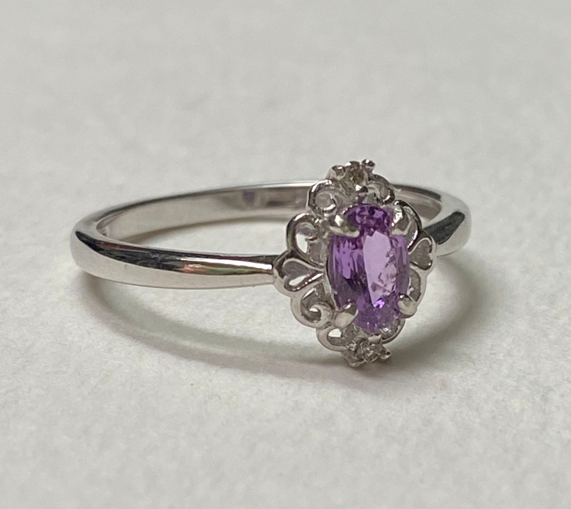 Sterling silver ring with oval pinkish-purple sapphire and diamond accents.