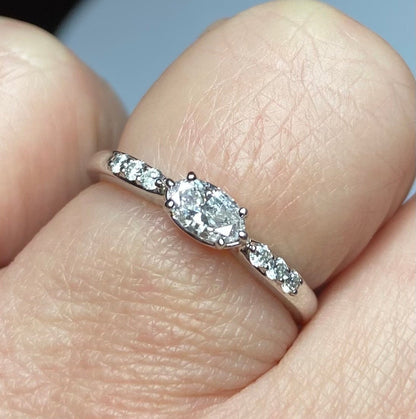 A white gold band ring with a marquise-shaped pink diamond center and small white diamonds.