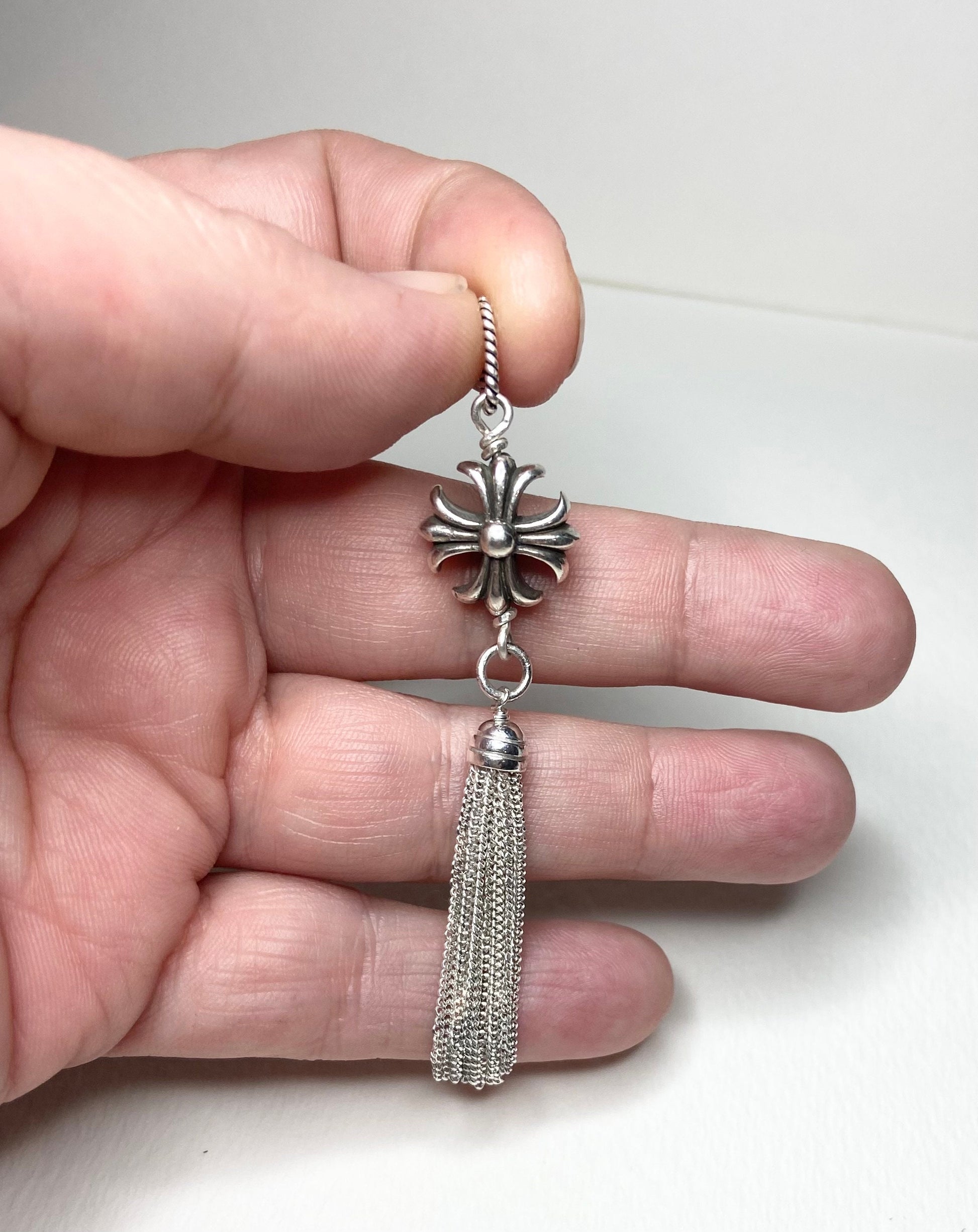 Sterling silver cross tassel pendant held by fingers.