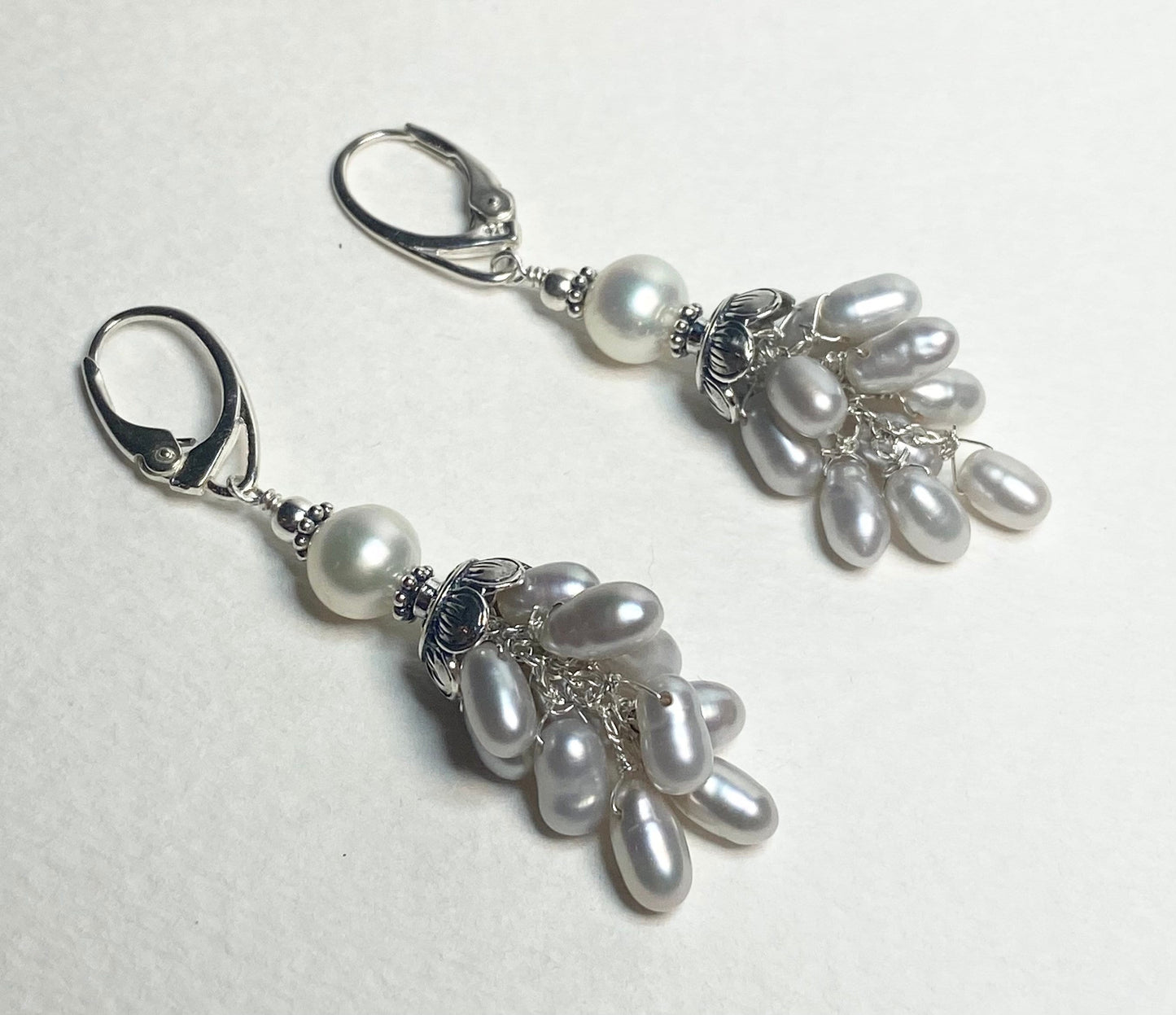 Silver dangle earrings with white and oval freshwater pearls.