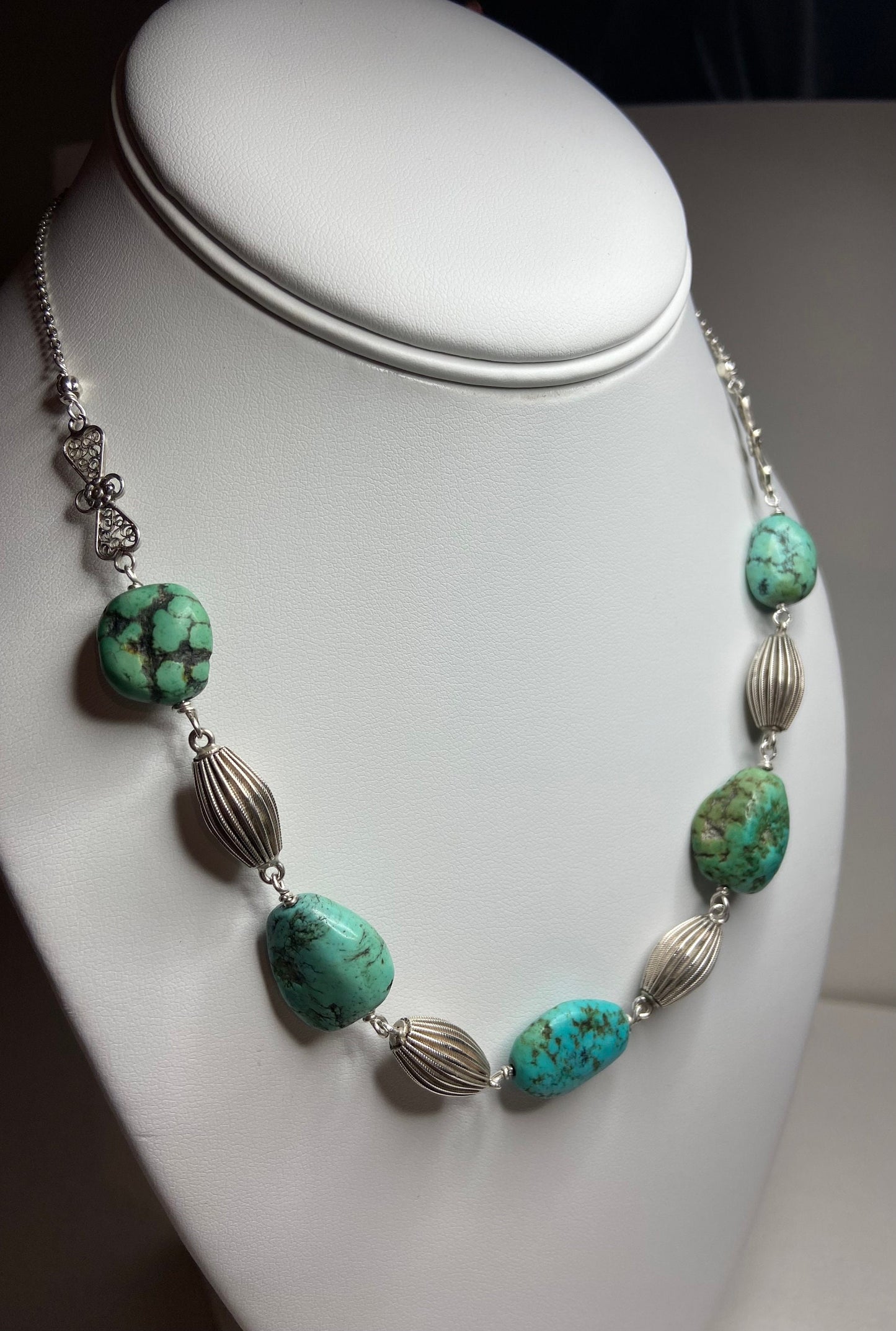 Turquoise beaded necklace with silver accents on a white display.