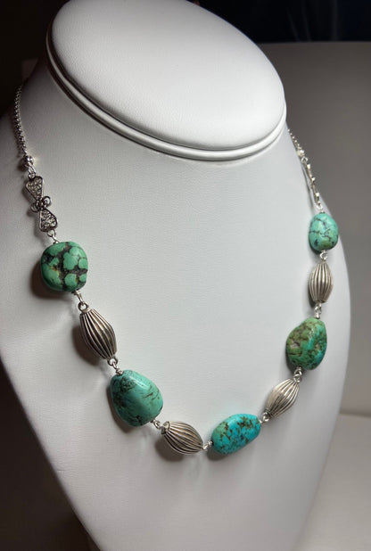 Turquoise beaded necklace with silver accents on a white display.