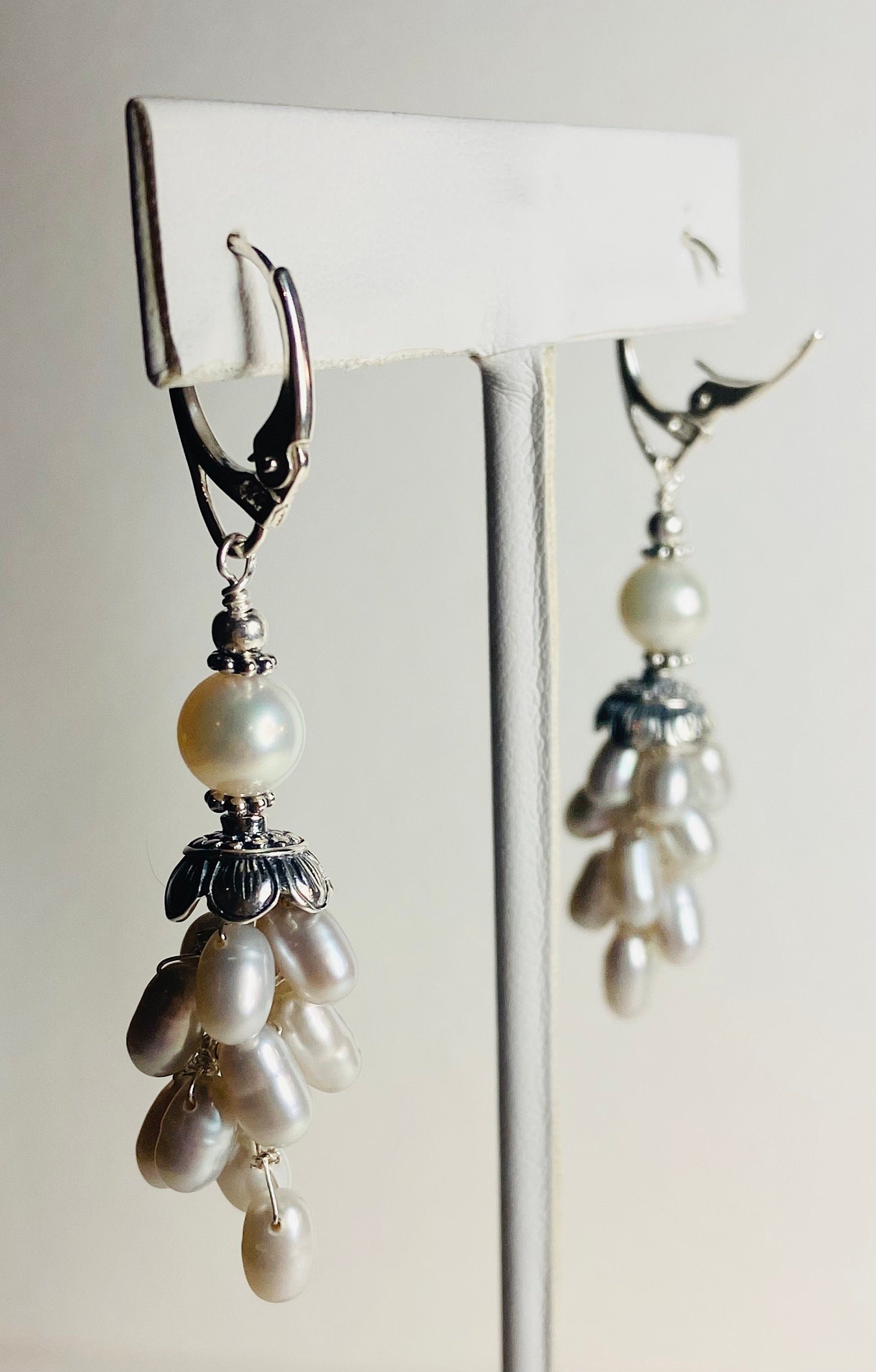 Silver dangle earrings with a large white pearl and a cluster of oval white pearls.