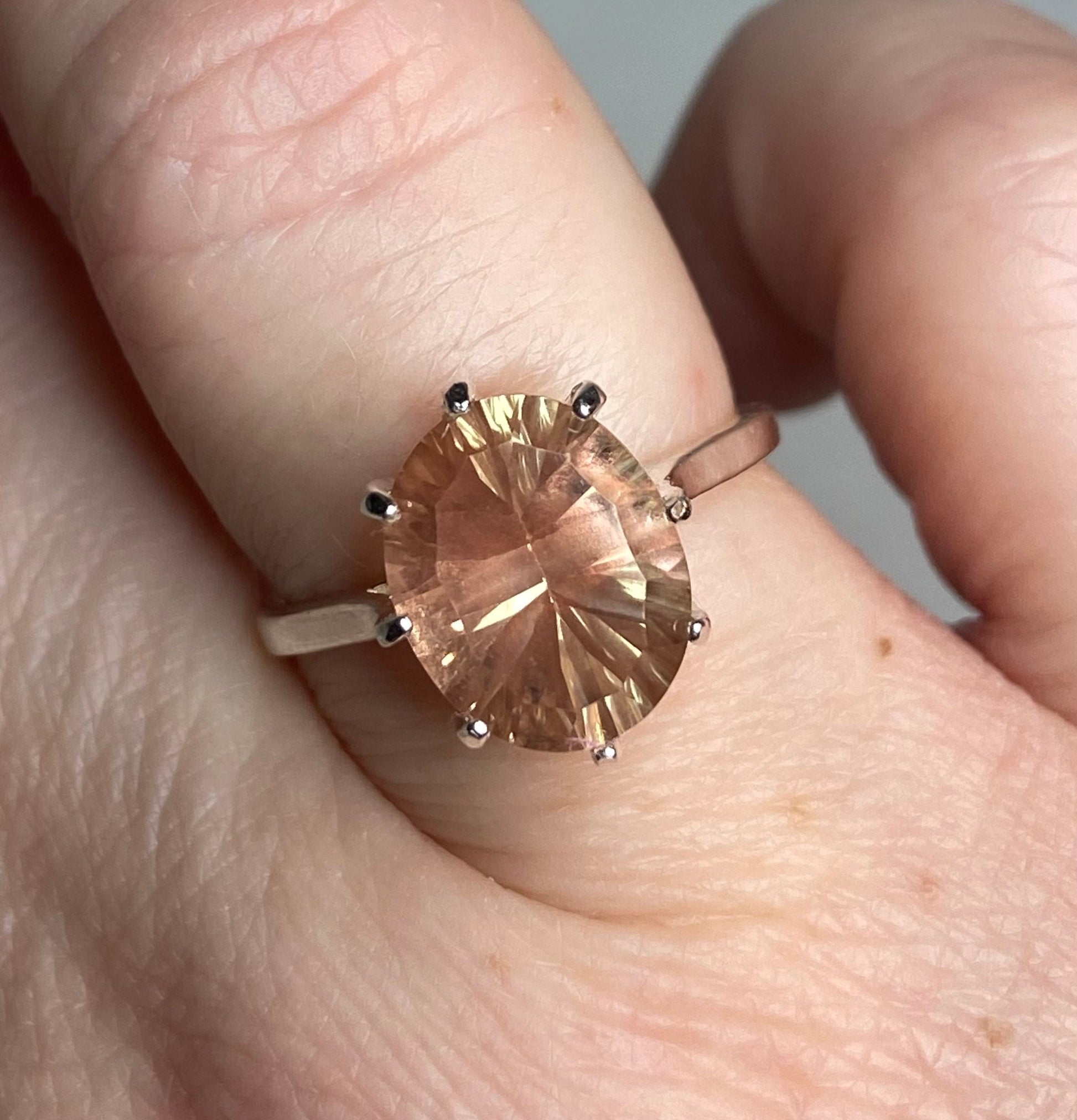 Sterling silver ring with a large oval Oregon sunstone featuring a concave cut and peach and greenish-yellow hues.