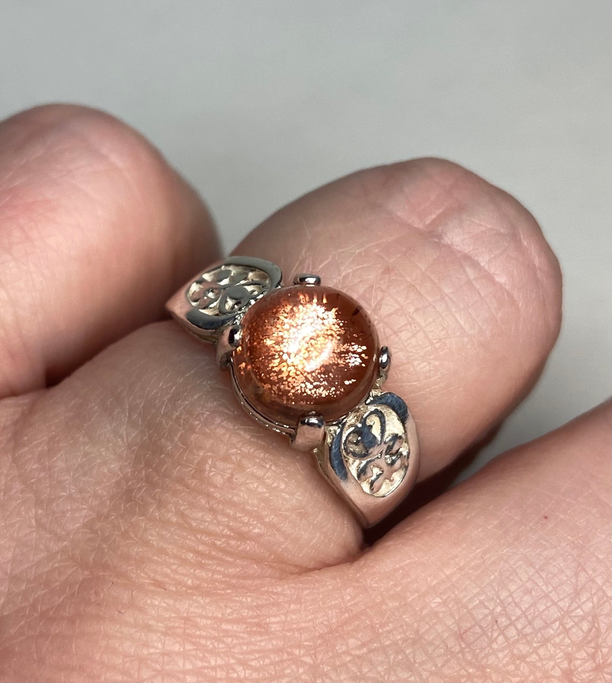 Sterling silver ring with a round Oregon sunstone cabochon and filigree band.