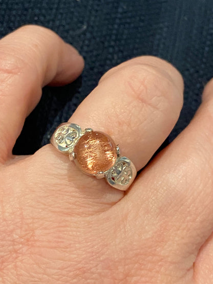 Sterling silver ring with a round Oregon sunstone cabochon and filigree accents.