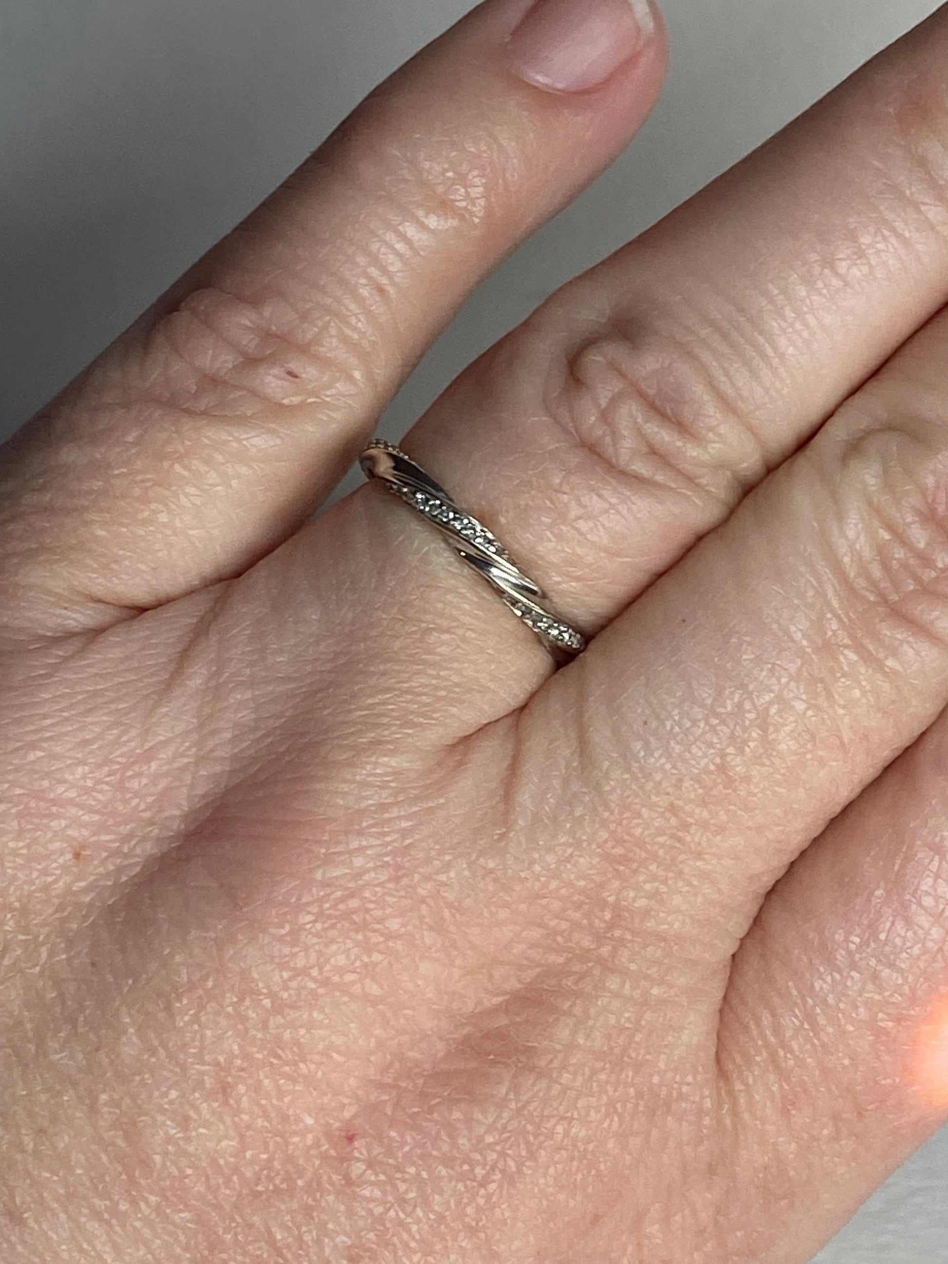 A 10k white gold eternity band with a twisted design and small diamonds.