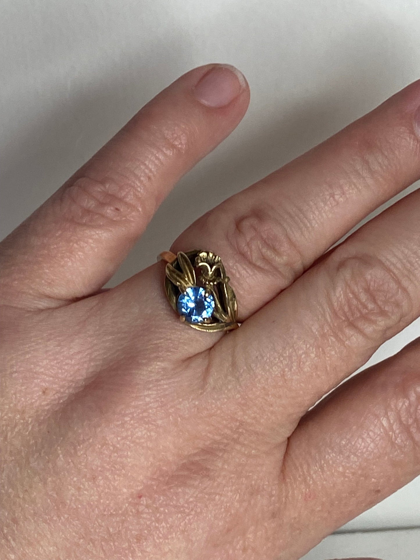 Art Nouveau style 10k yellow gold ring with a blue spinel and floral motif.