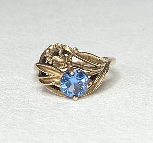 Art Nouveau style 10k yellow gold ring with a blue synthetic spinel and floral motif.