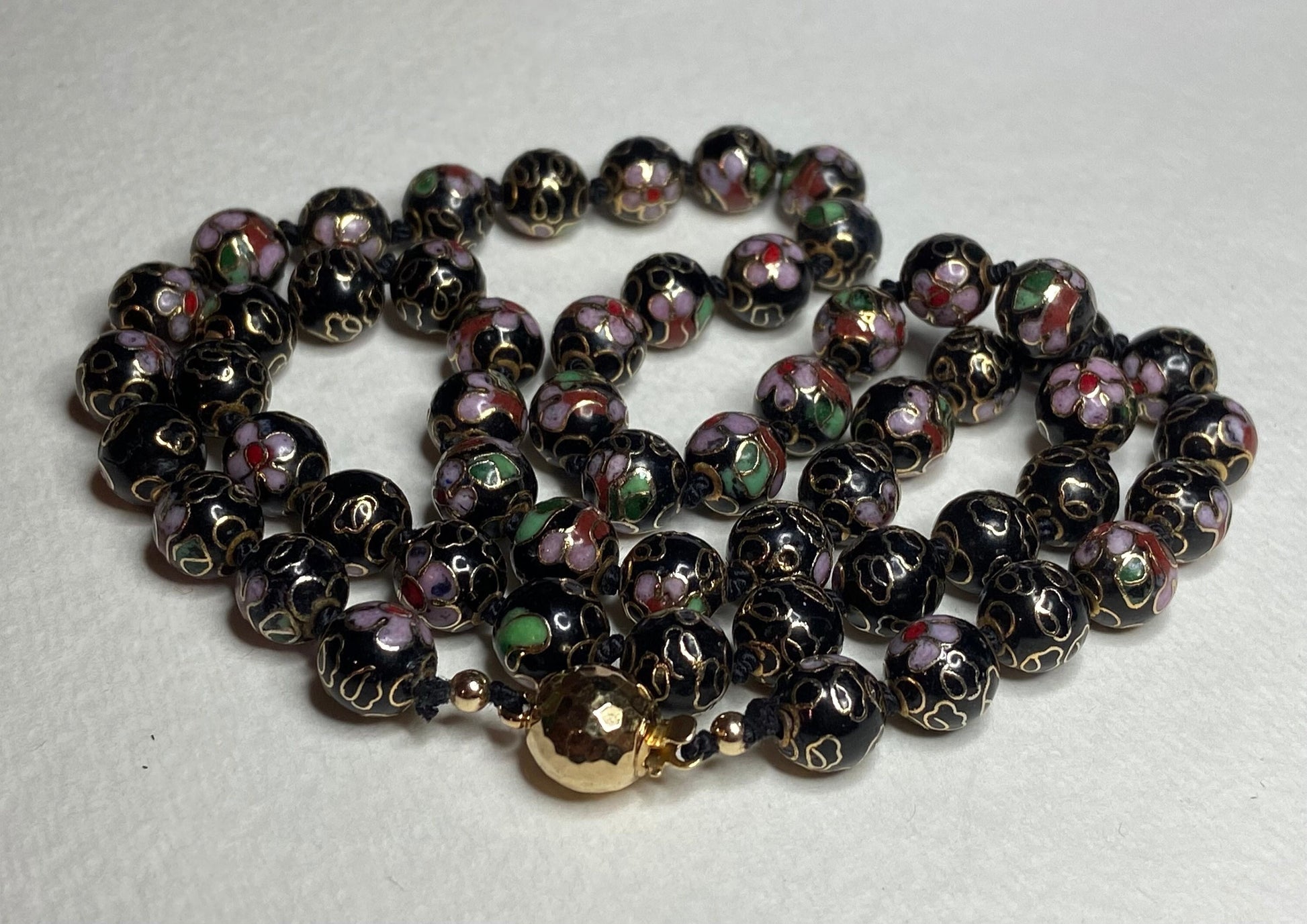 Cloisonné beaded necklace with black, pink, and gold floral designs and a gold clasp.