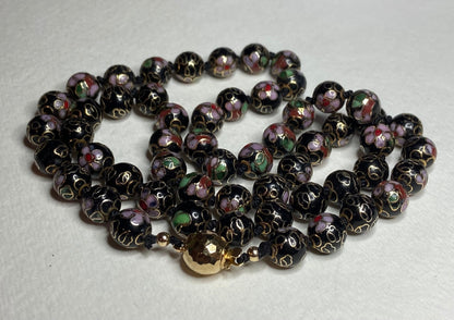 Cloisonné beaded necklace with black, pink, and gold floral designs and a gold clasp.