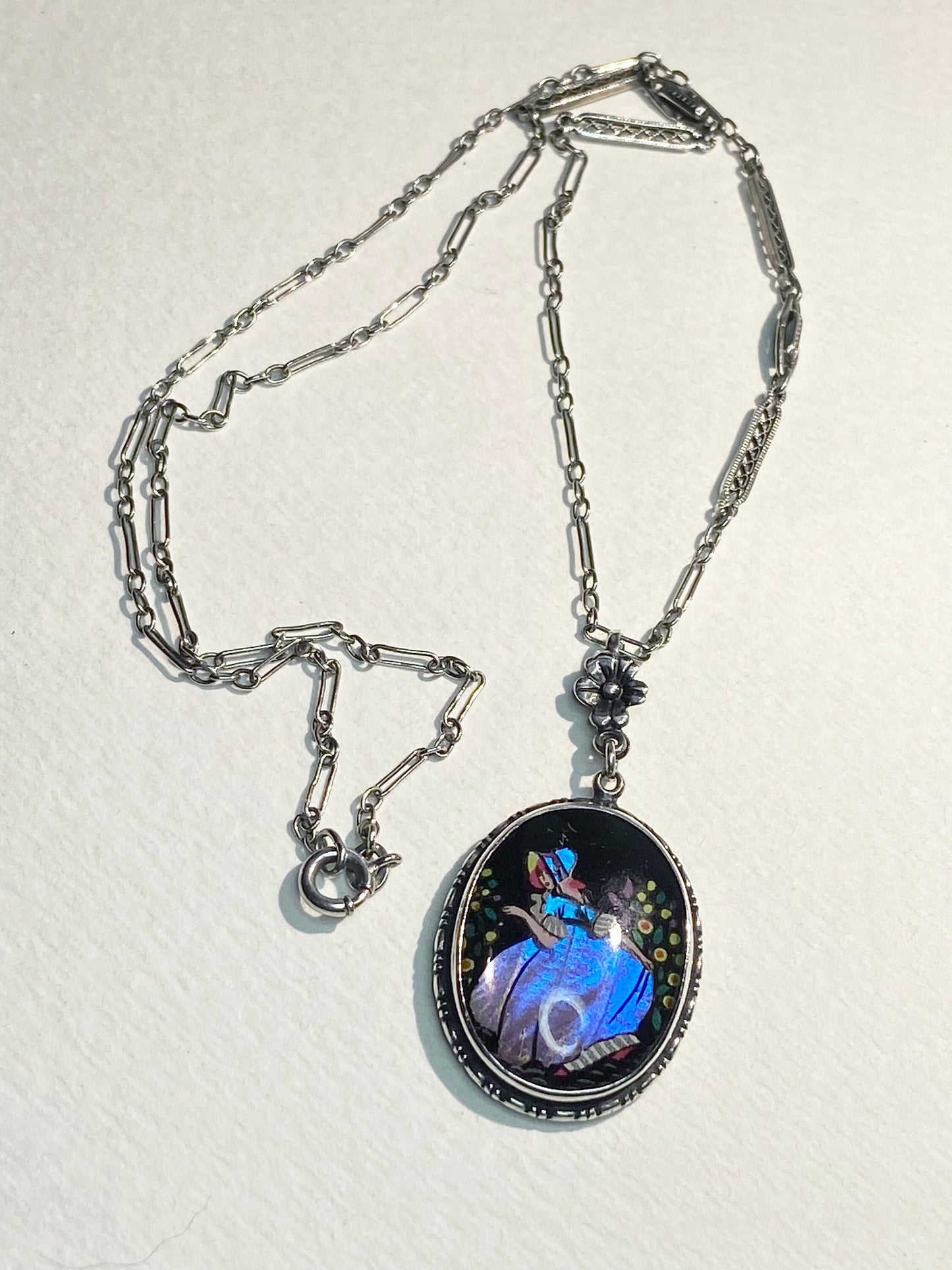 Sterling silver necklace with an oval pendant featuring a reverse-painted Morpho butterfly wing and a lady in a garden.