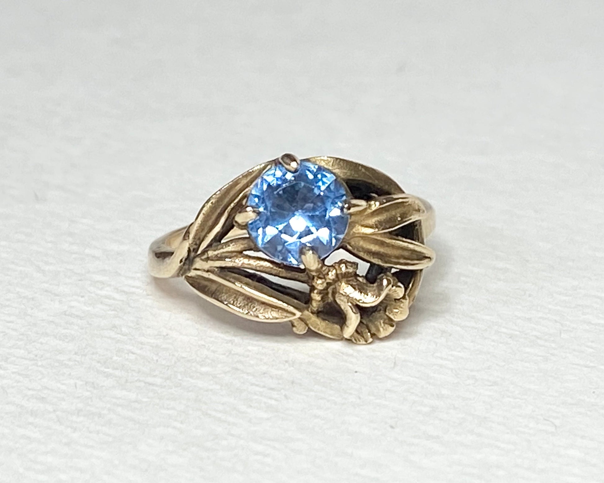 Art Nouveau style 10k yellow gold ring with a blue spinel and floral motif.