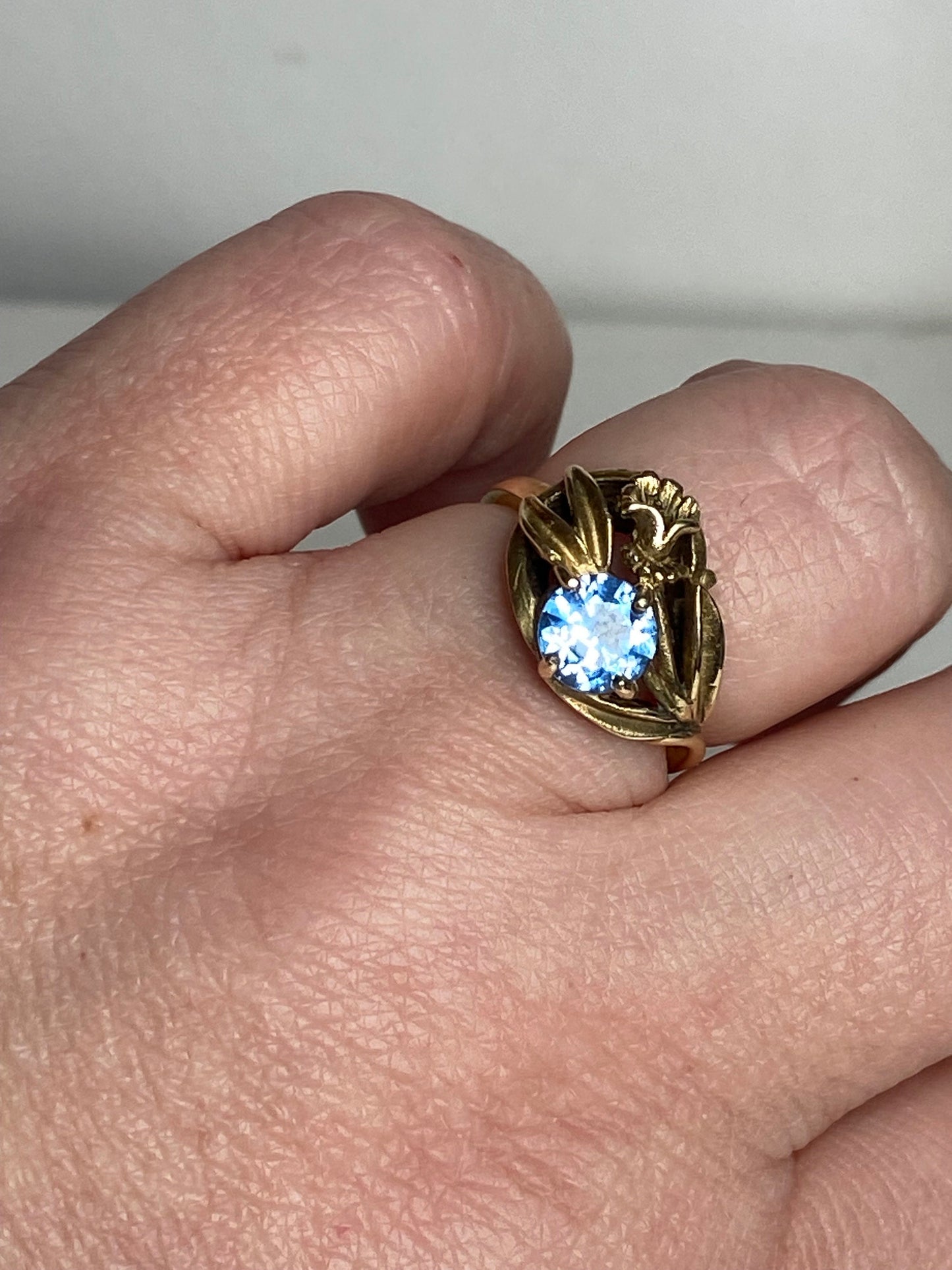Art Nouveau style 10k yellow gold ring with a blue synthetic spinel and floral motif.
