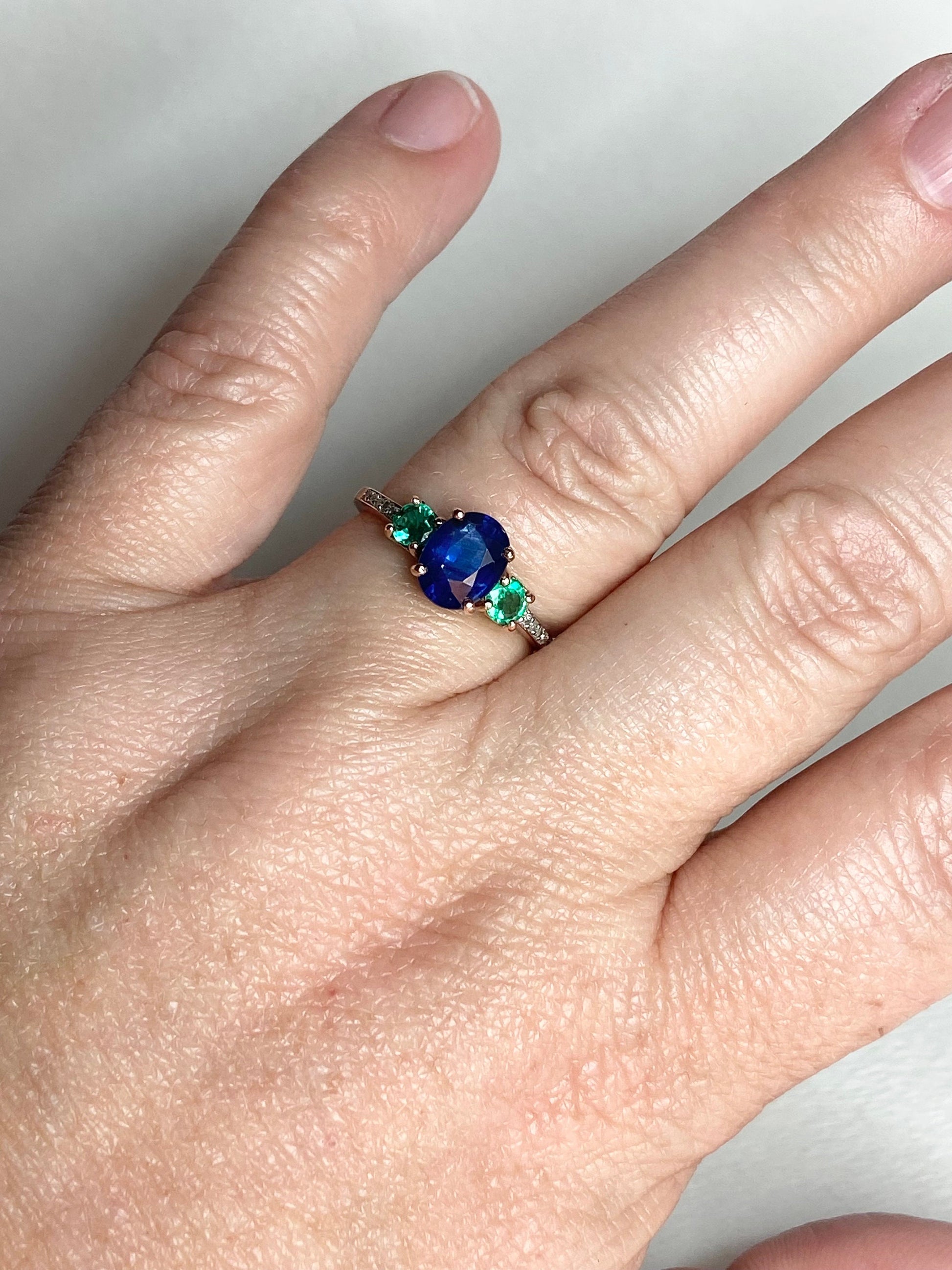 Oval blue sapphire ring with emeralds and diamonds in rose gold.