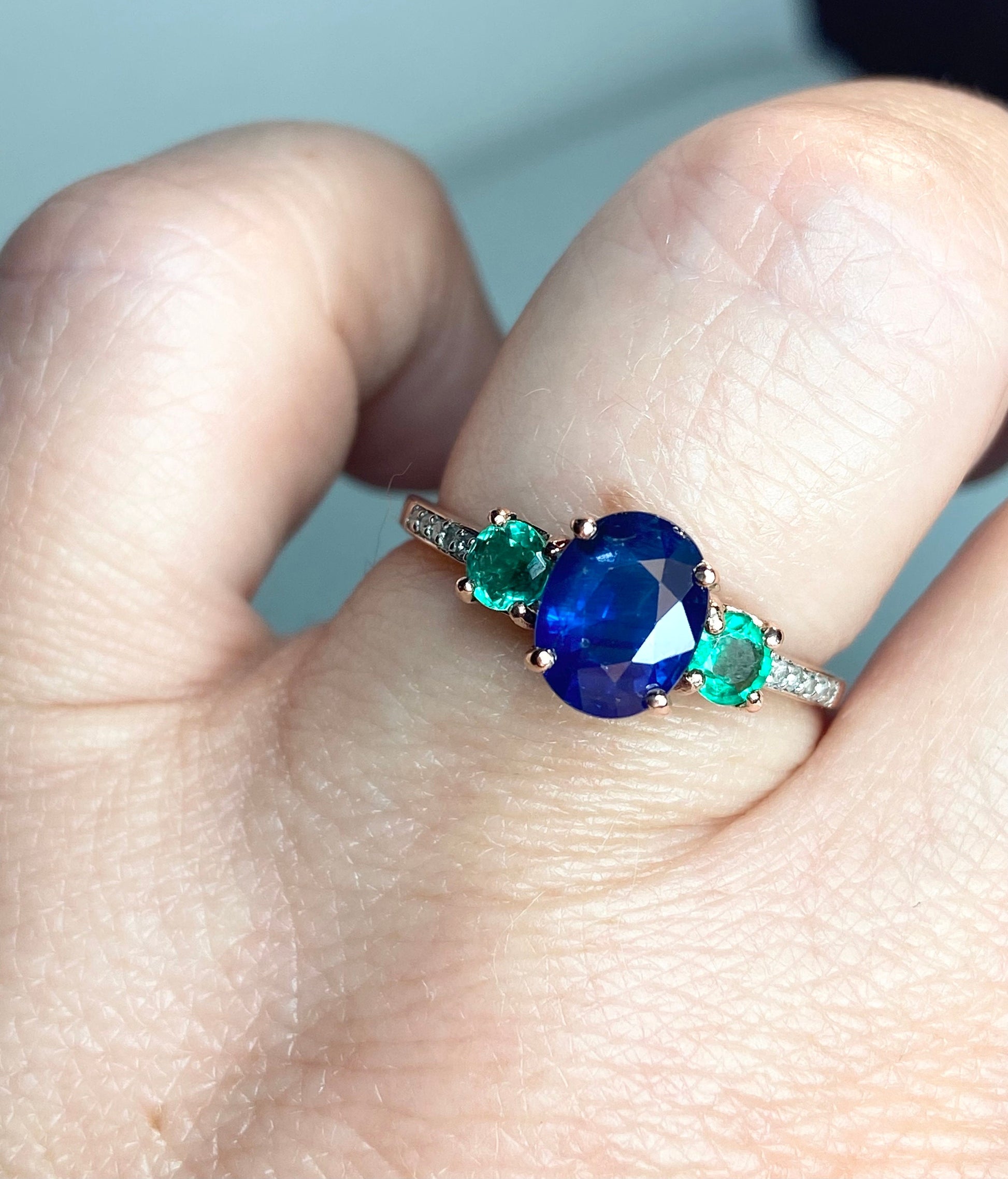 Oval blue sapphire ring with emeralds and diamonds in rose gold.