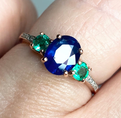 Oval blue sapphire ring with emeralds and diamonds in rose gold.