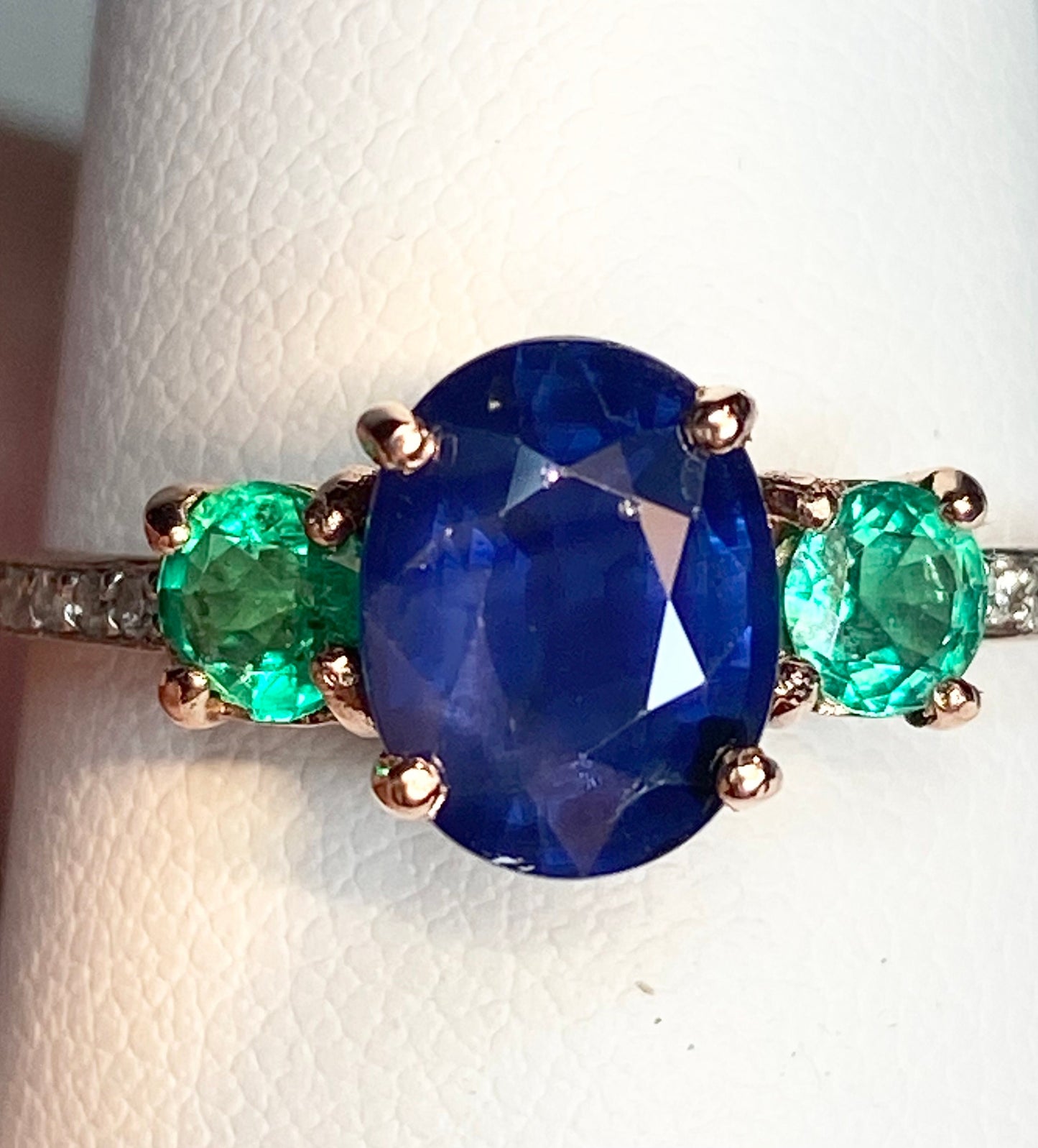 Oval blue sapphire ring with emeralds and diamonds in rose gold.
