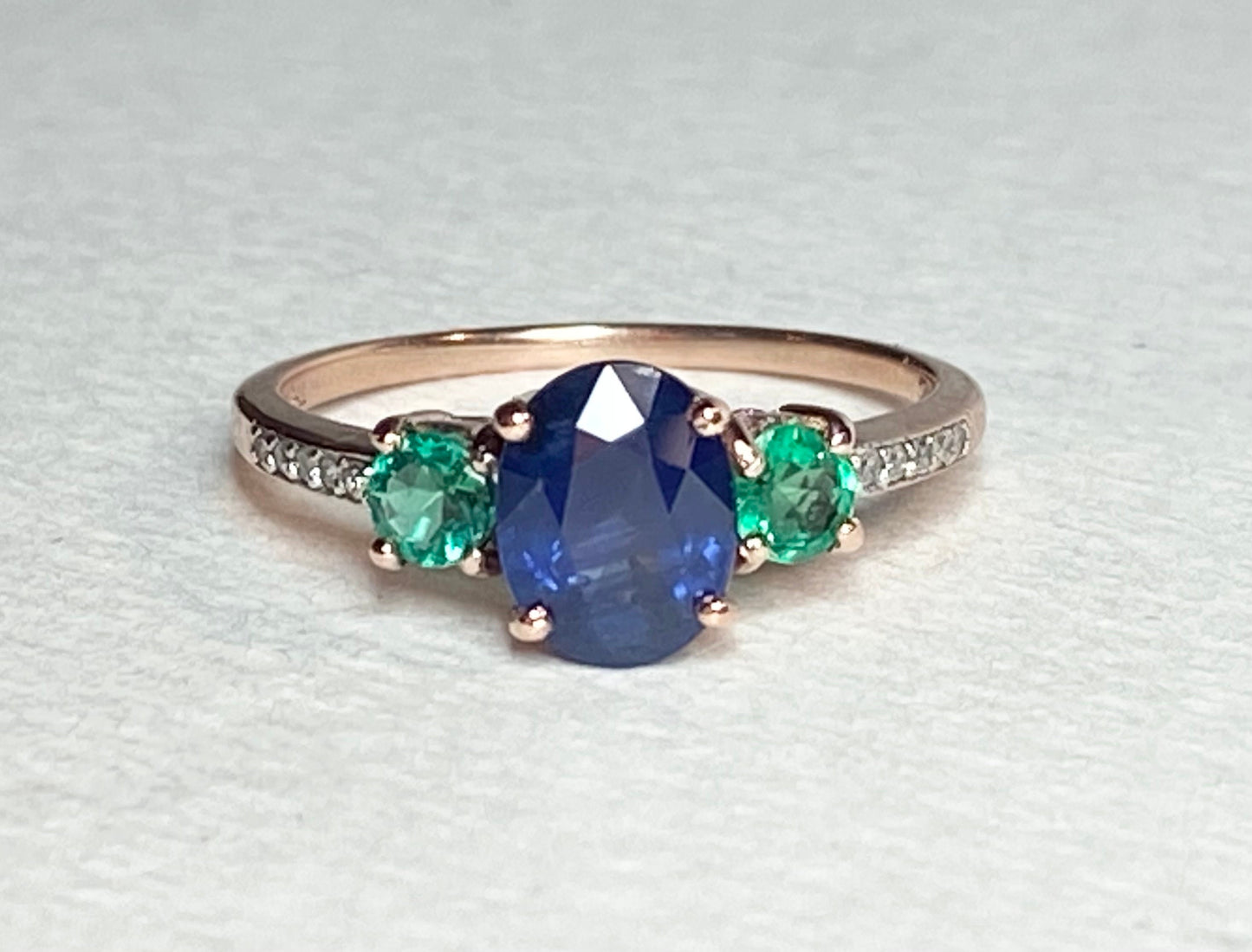 Oval blue sapphire ring with emeralds and diamonds in rose gold.