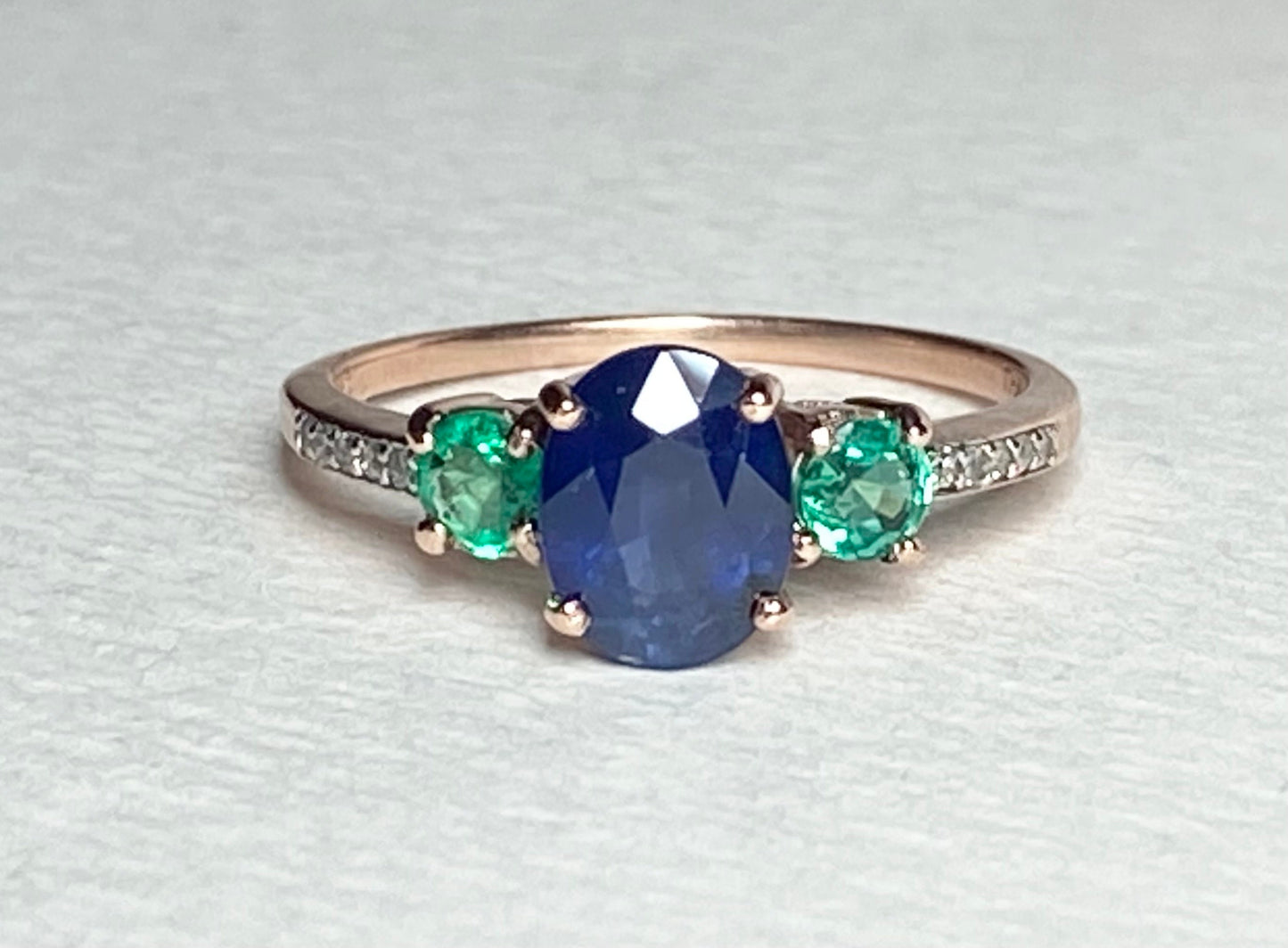 Oval blue sapphire ring with emeralds and diamonds in rose gold.