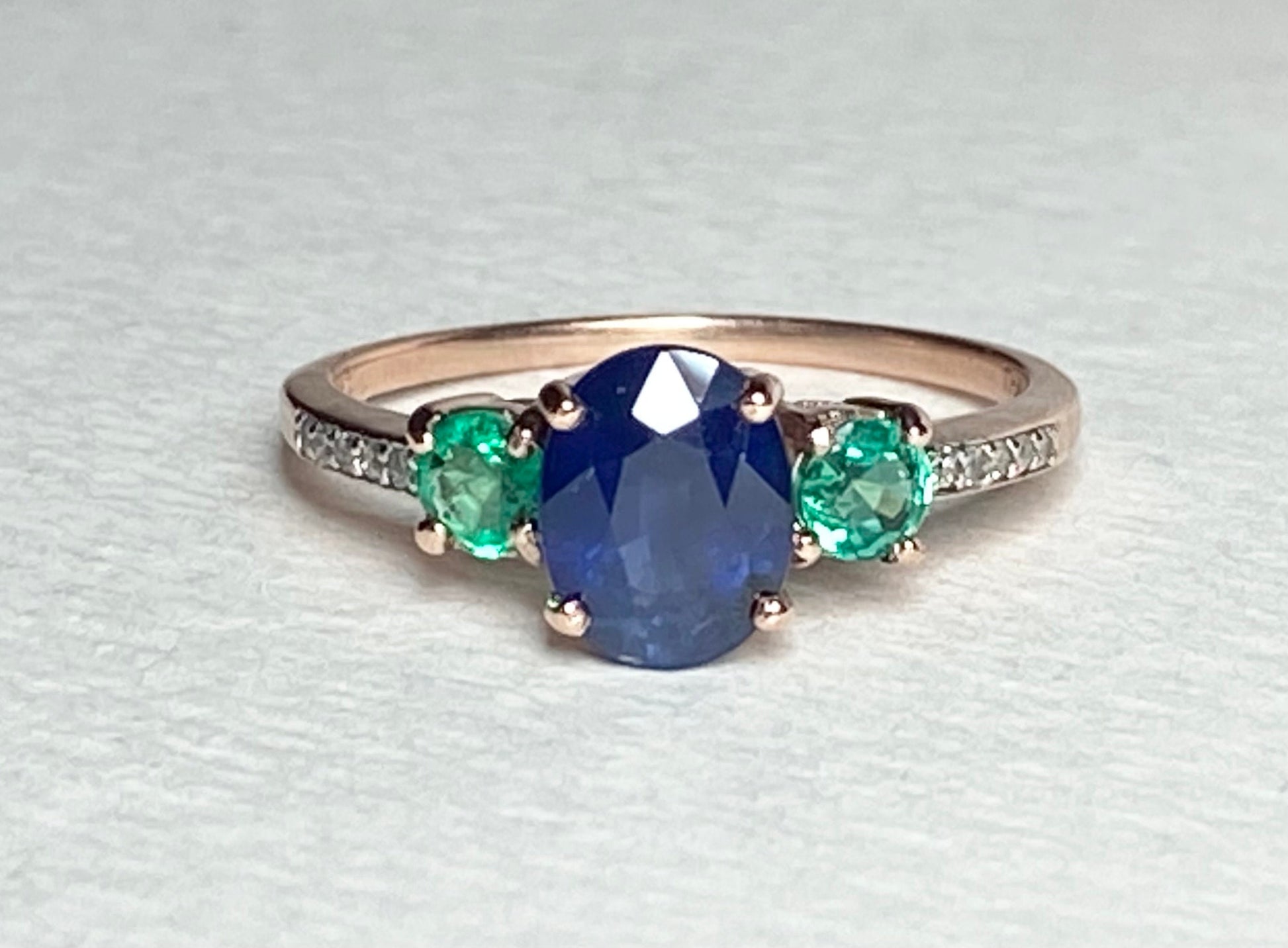 Oval blue sapphire ring with emeralds and diamonds in rose gold.