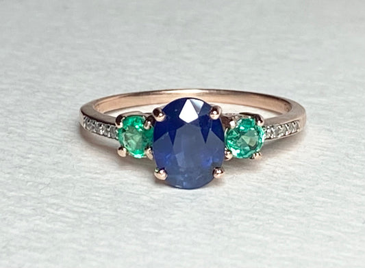 Oval blue sapphire ring with emeralds and diamonds in rose gold.