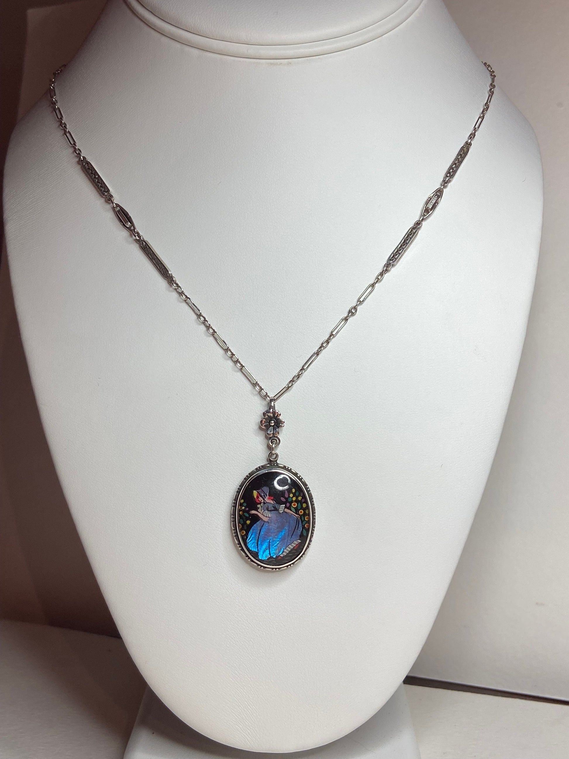 Sterling silver necklace with oval pendant featuring a reverse-painted butterfly wing of a red-haired lady in a garden.