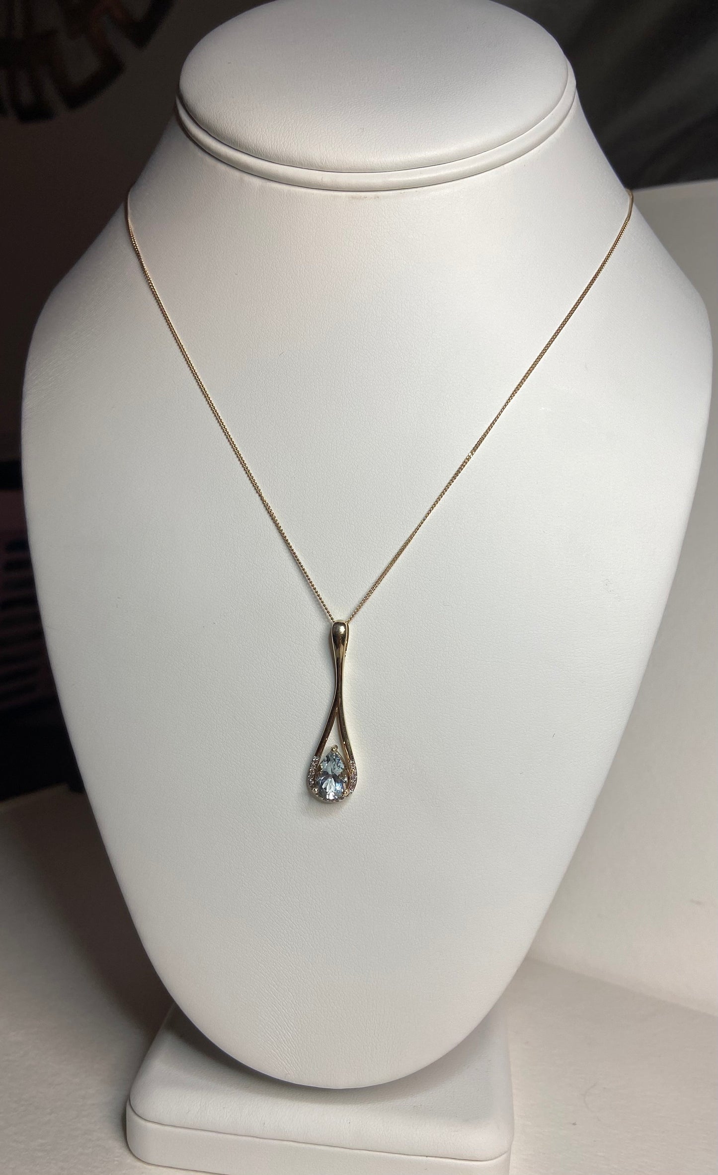 A pear-shaped aquamarine and diamond pendant on a gold necklace.