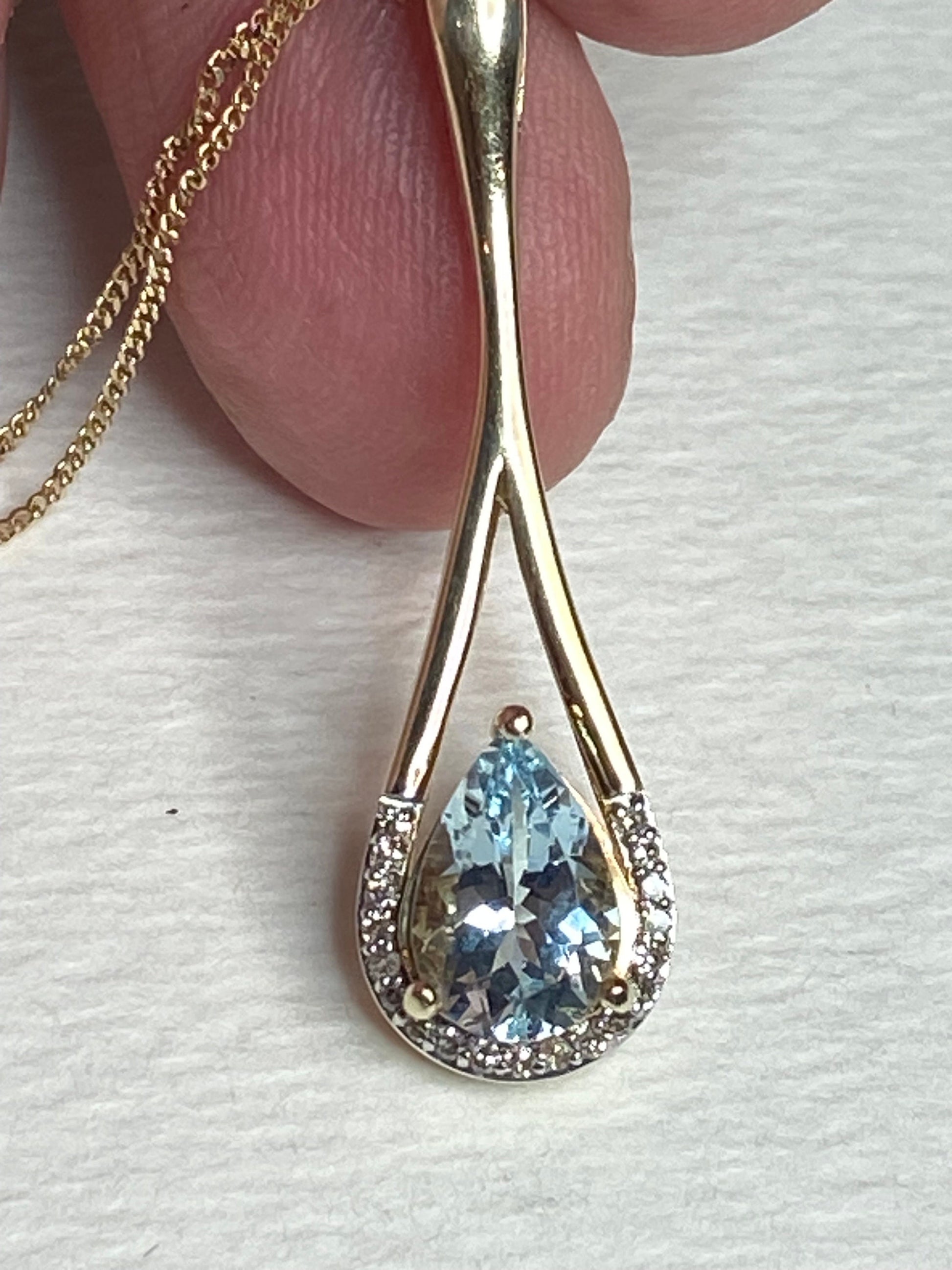 A pear-shaped aquamarine pendant with diamonds on a gold chain.