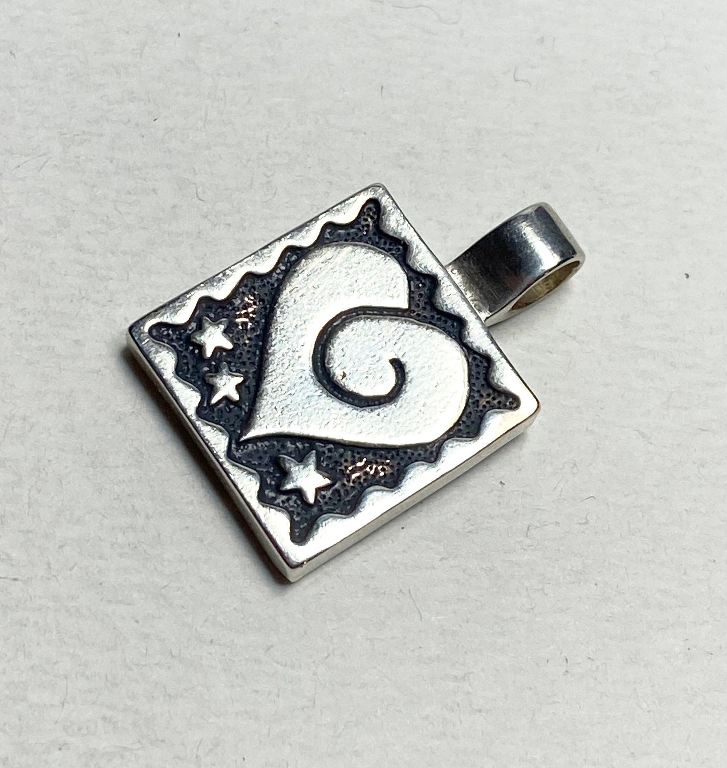 Sterling silver square pendant with a heart and stars design.
