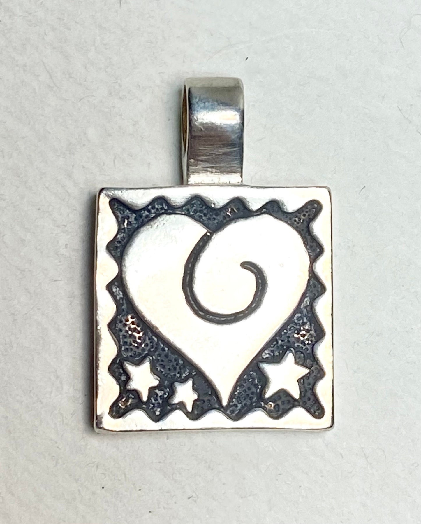 Sterling silver square pendant with a heart and stars design.
