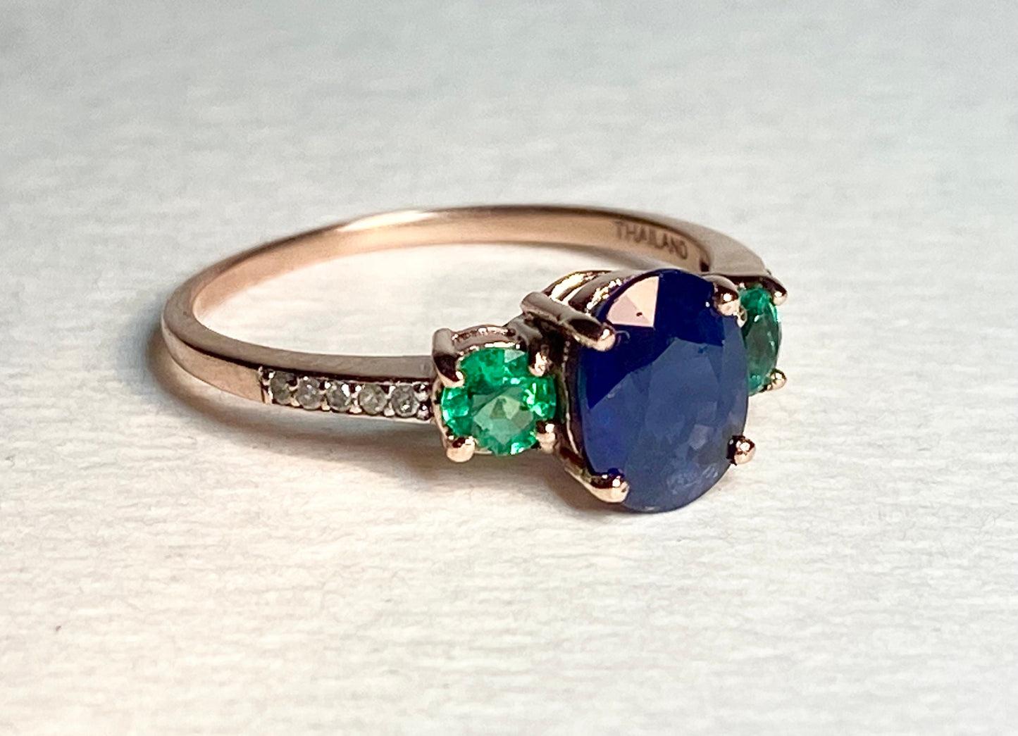 Ring with blue sapphire, emeralds, and diamonds in rose gold.