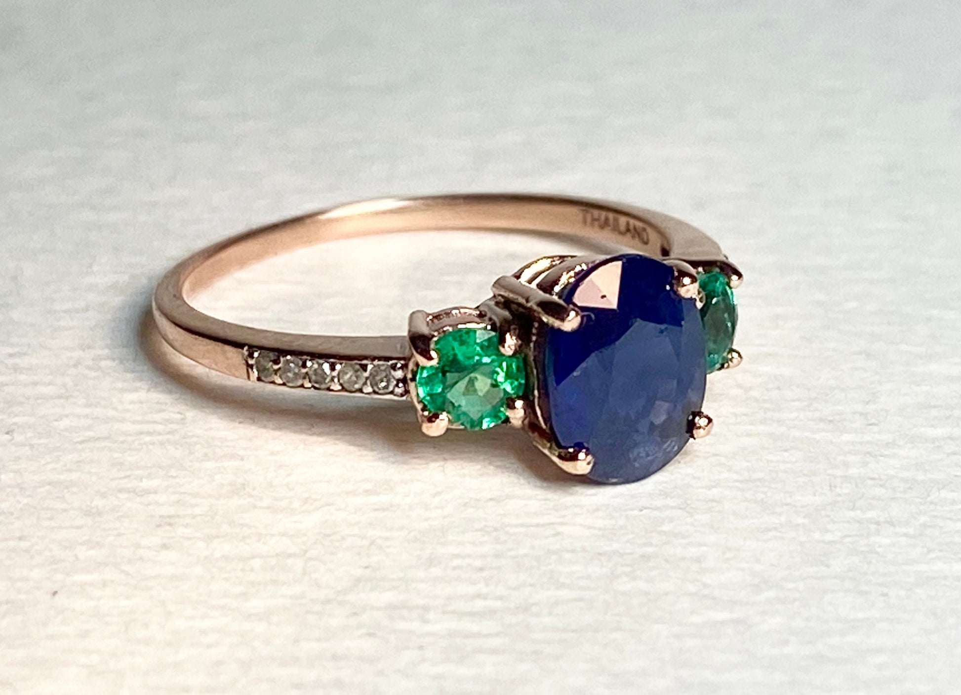 Ring with blue sapphire, emeralds, and diamonds in rose gold.