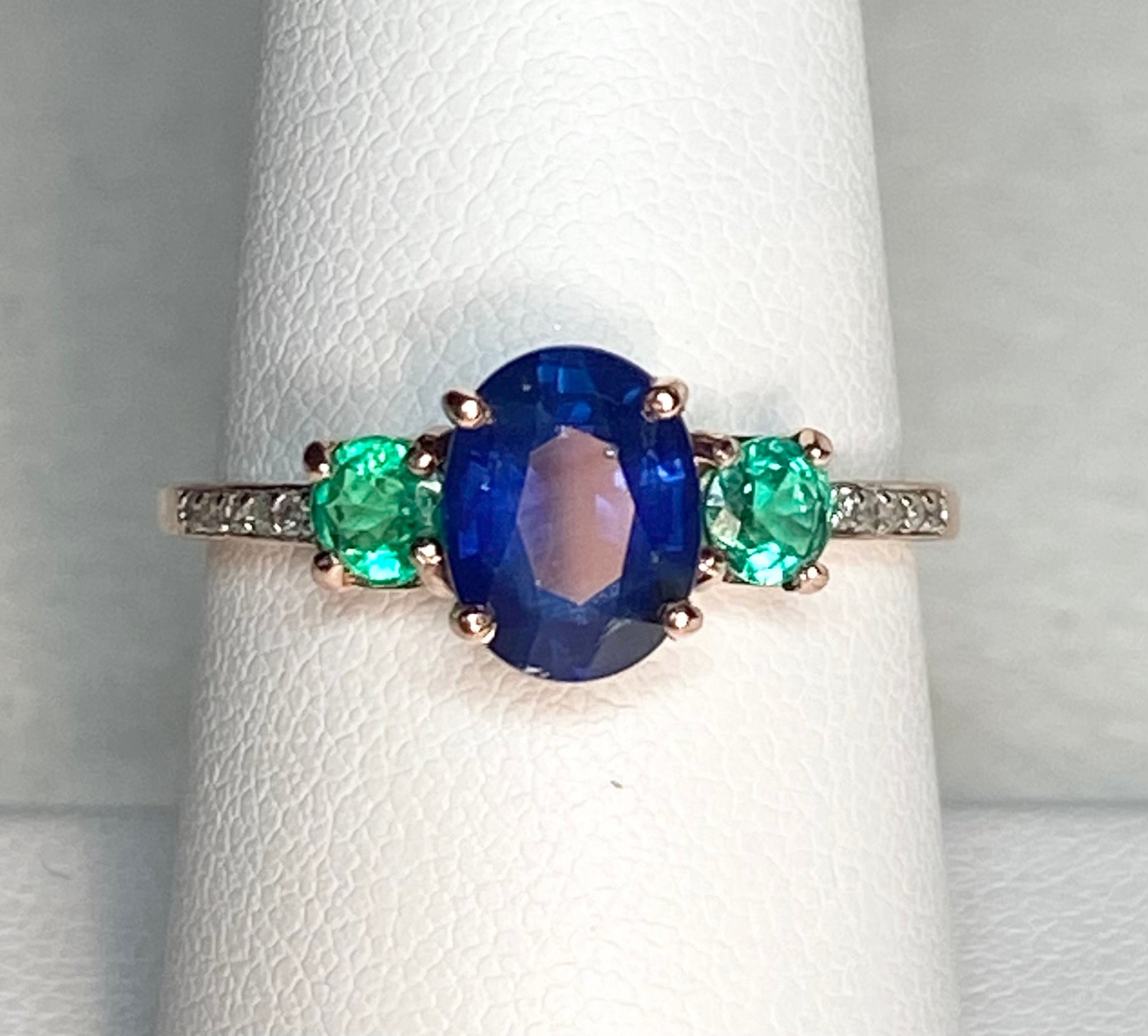Oval blue sapphire ring with emeralds and diamonds in rose gold.