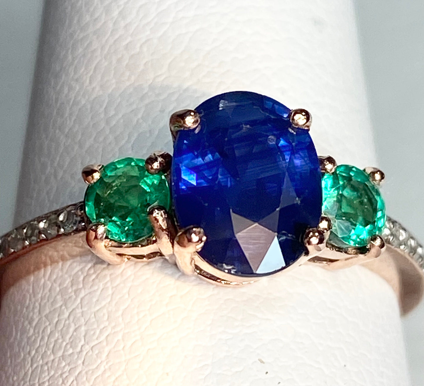 Oval blue sapphire ring with emeralds and diamonds in rose gold.