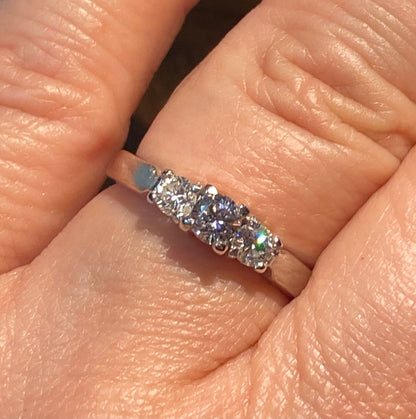 Platinum ring with three diamonds, including a very light pink center stone.