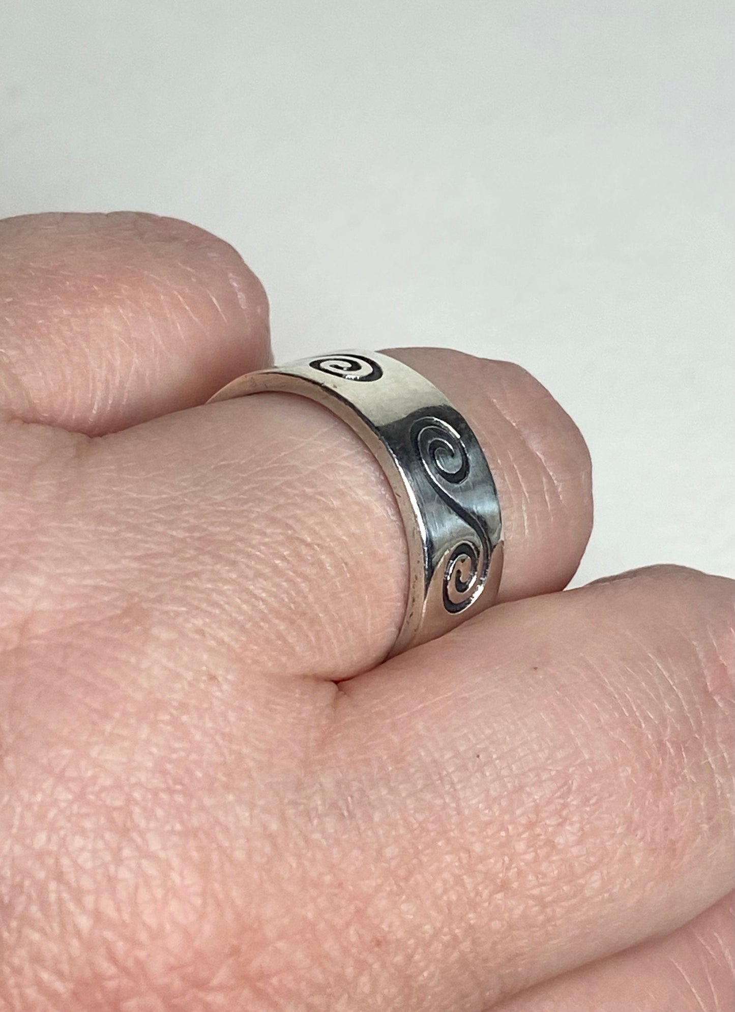An 8mm wide sterling silver band ring with a swirl design.