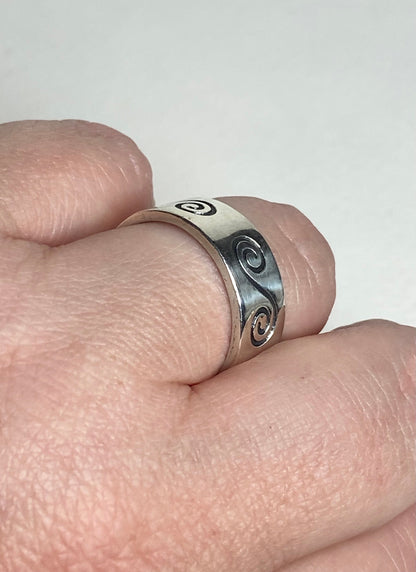 An 8mm wide sterling silver band ring with a swirl design.