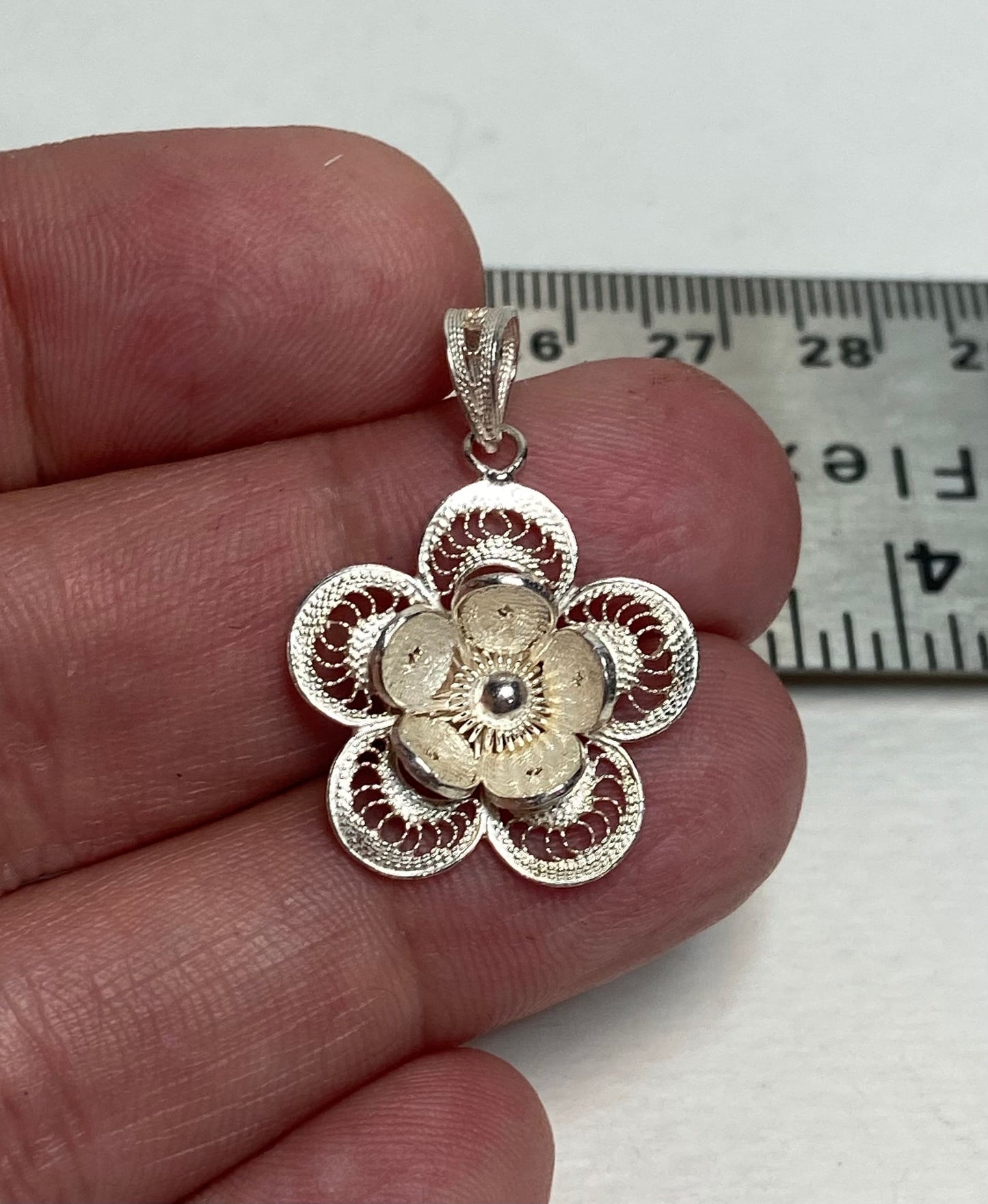 Sterling silver filigree flower pendant held by fingers.