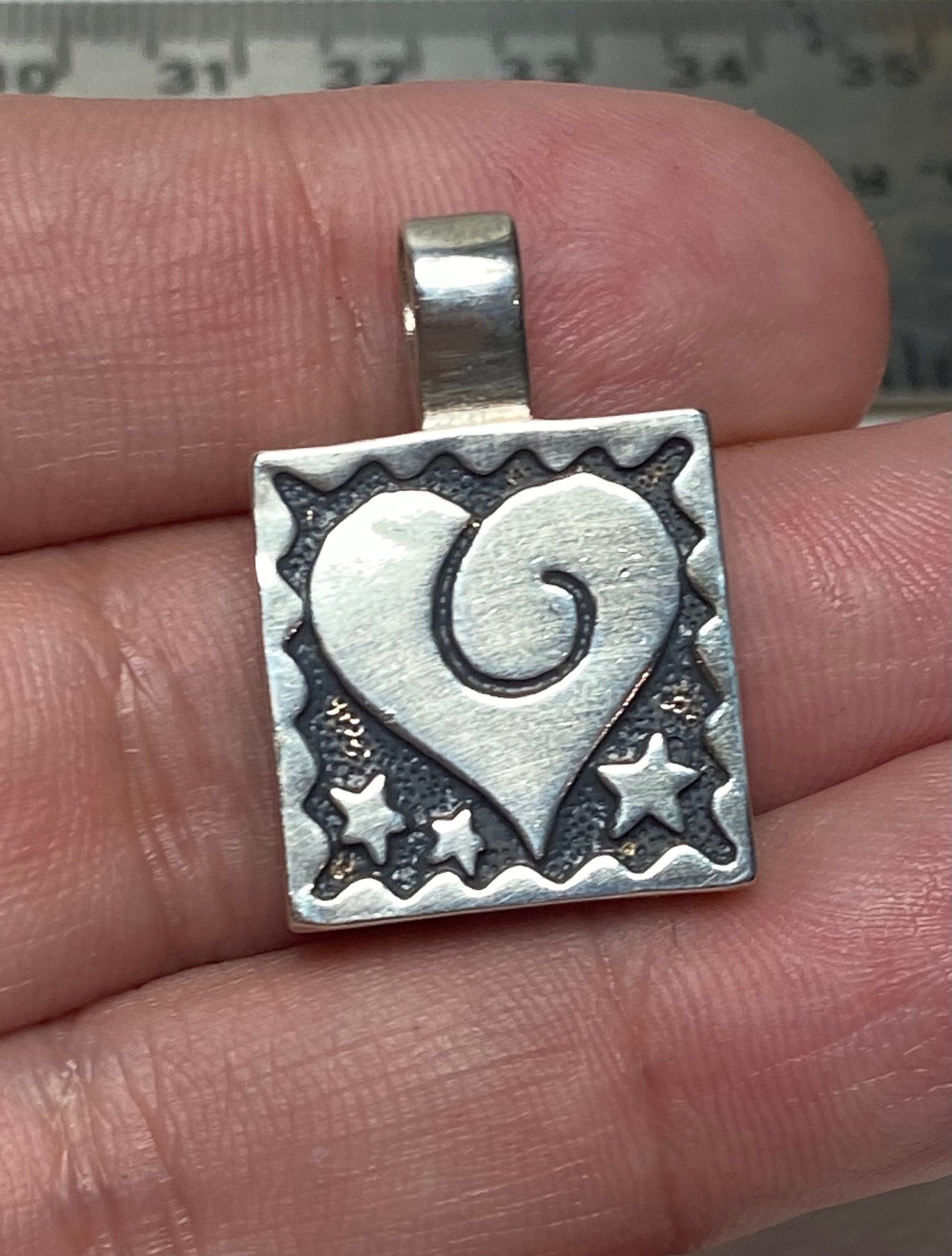 Sterling silver square pendant with a heart and stars design.