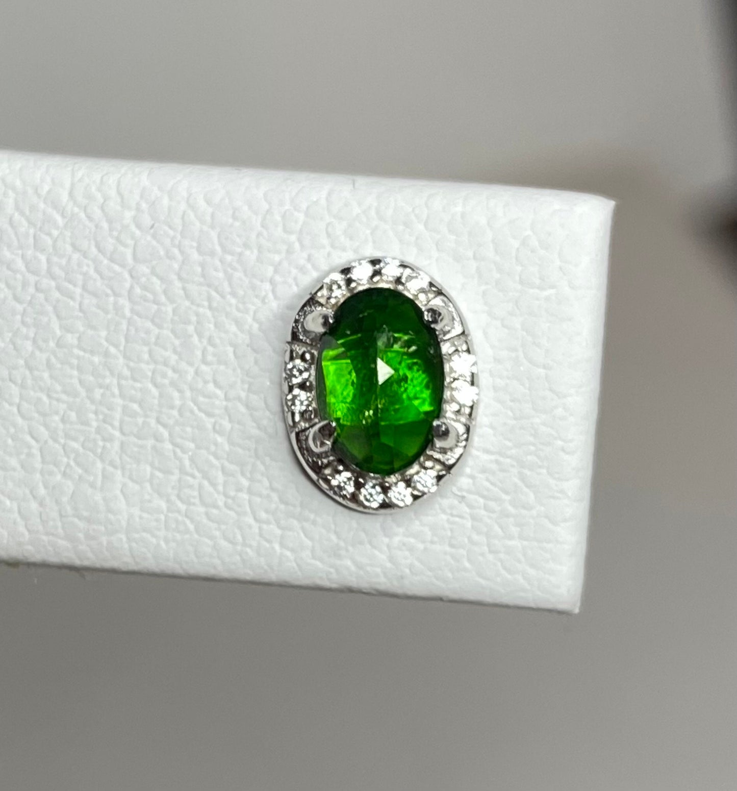 Sterling silver stud earrings featuring an oval chrome diopside gemstone surrounded by small cubic zirconia stones.