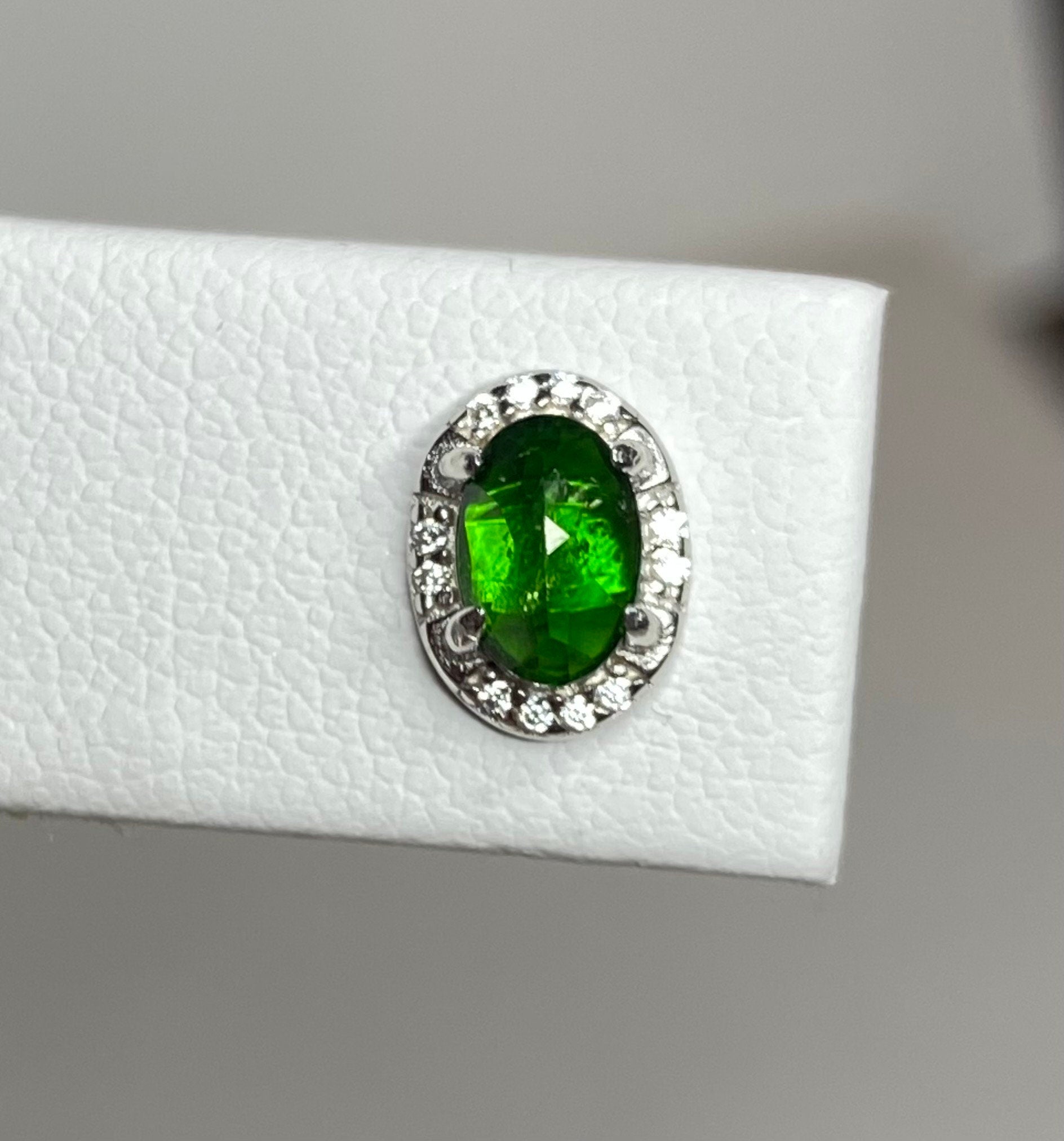 Sterling silver stud earrings featuring an oval chrome diopside gemstone surrounded by small cubic zirconia stones.