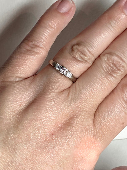 Platinum ring with three diamonds, including a very light pink center stone.