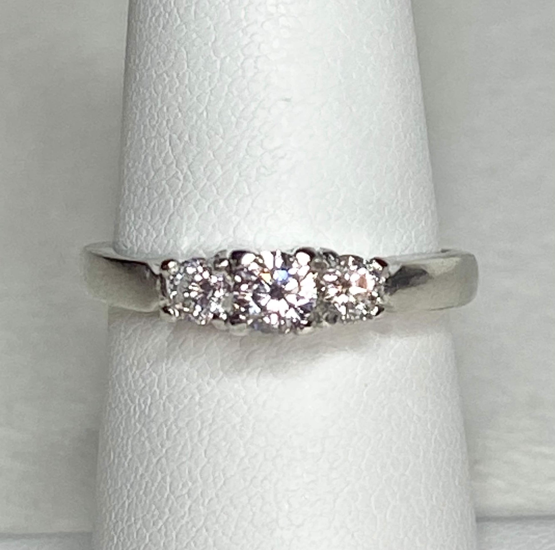 Platinum ring with three diamonds, including a very light pink center stone.
