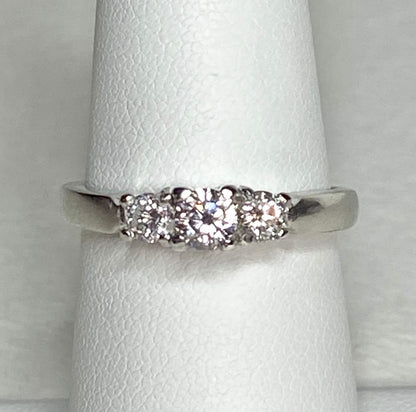 Platinum ring with three diamonds, including a very light pink center stone.