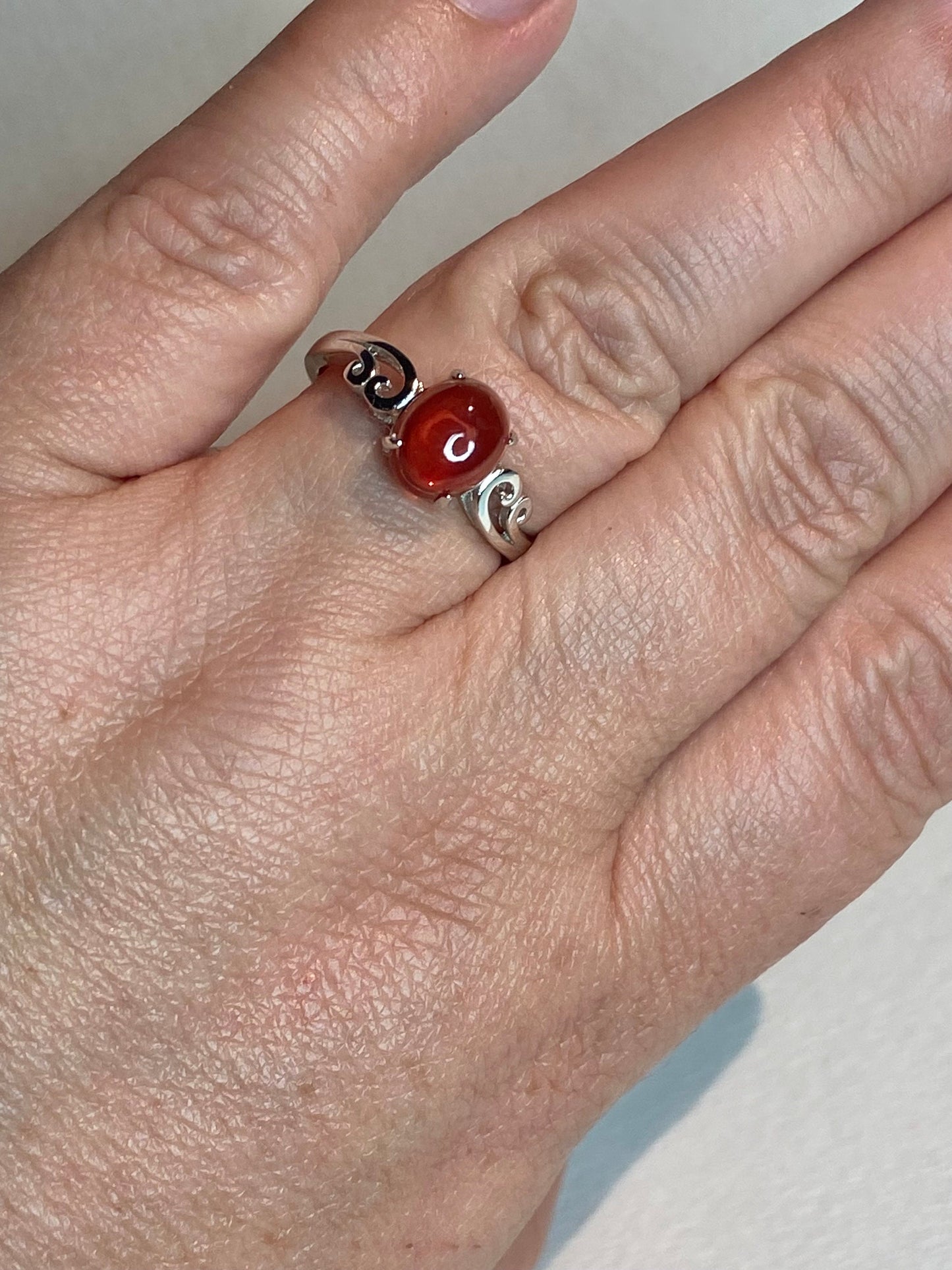 Sterling silver ring with a red Oregon sunstone cabochon and swirl details.