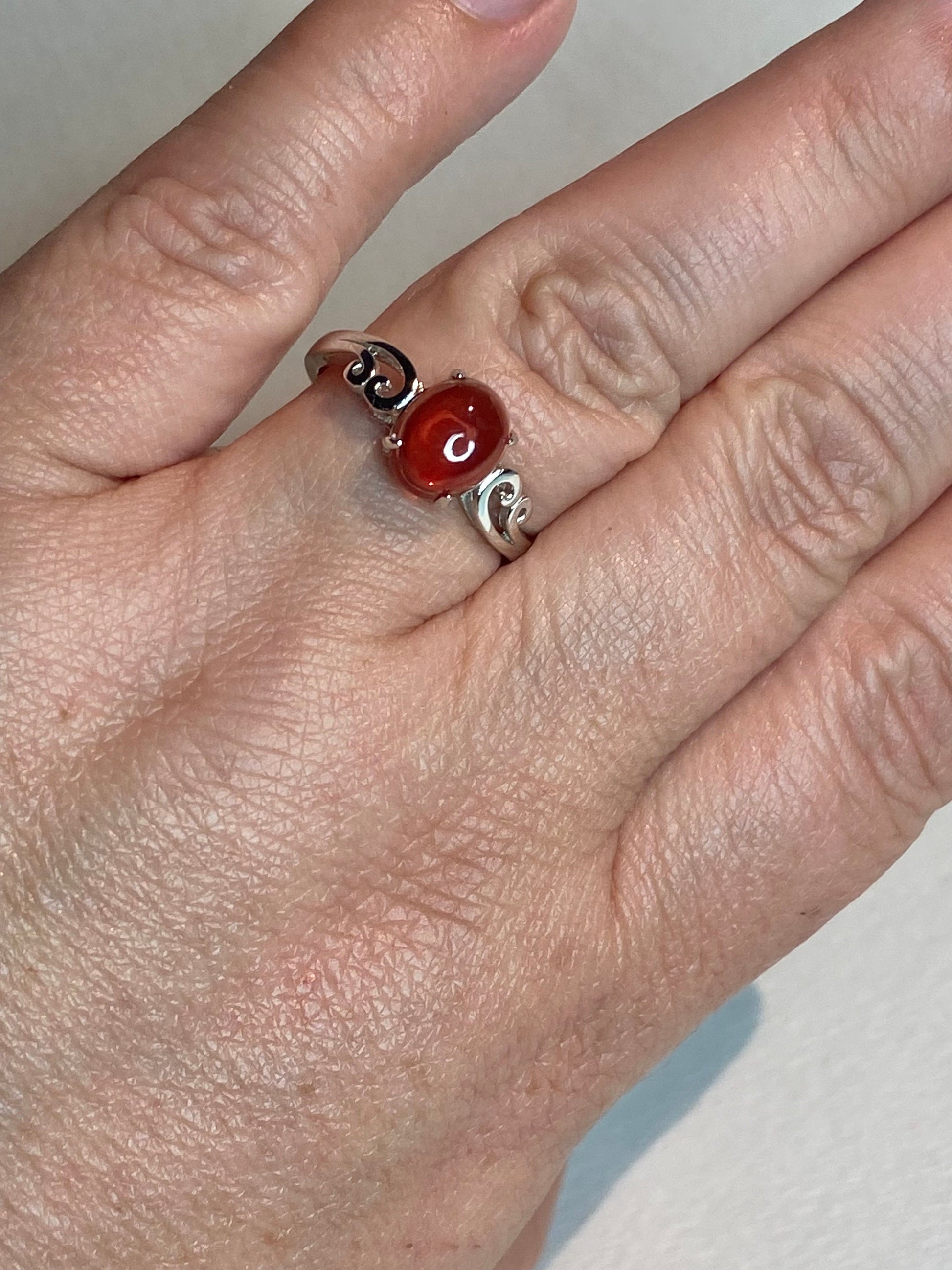 Sterling silver ring with a red Oregon sunstone cabochon and swirl details.