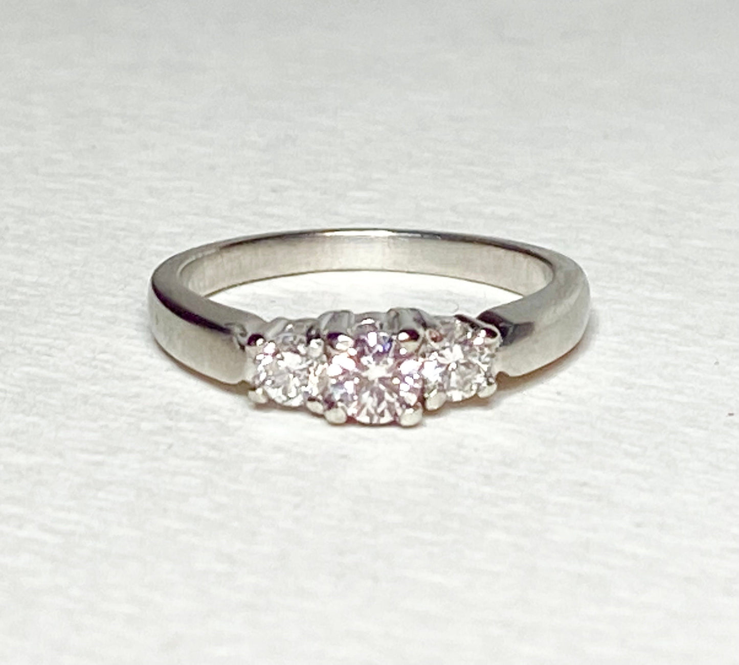 Platinum three-stone ring with a light pink diamond center and two white diamonds.