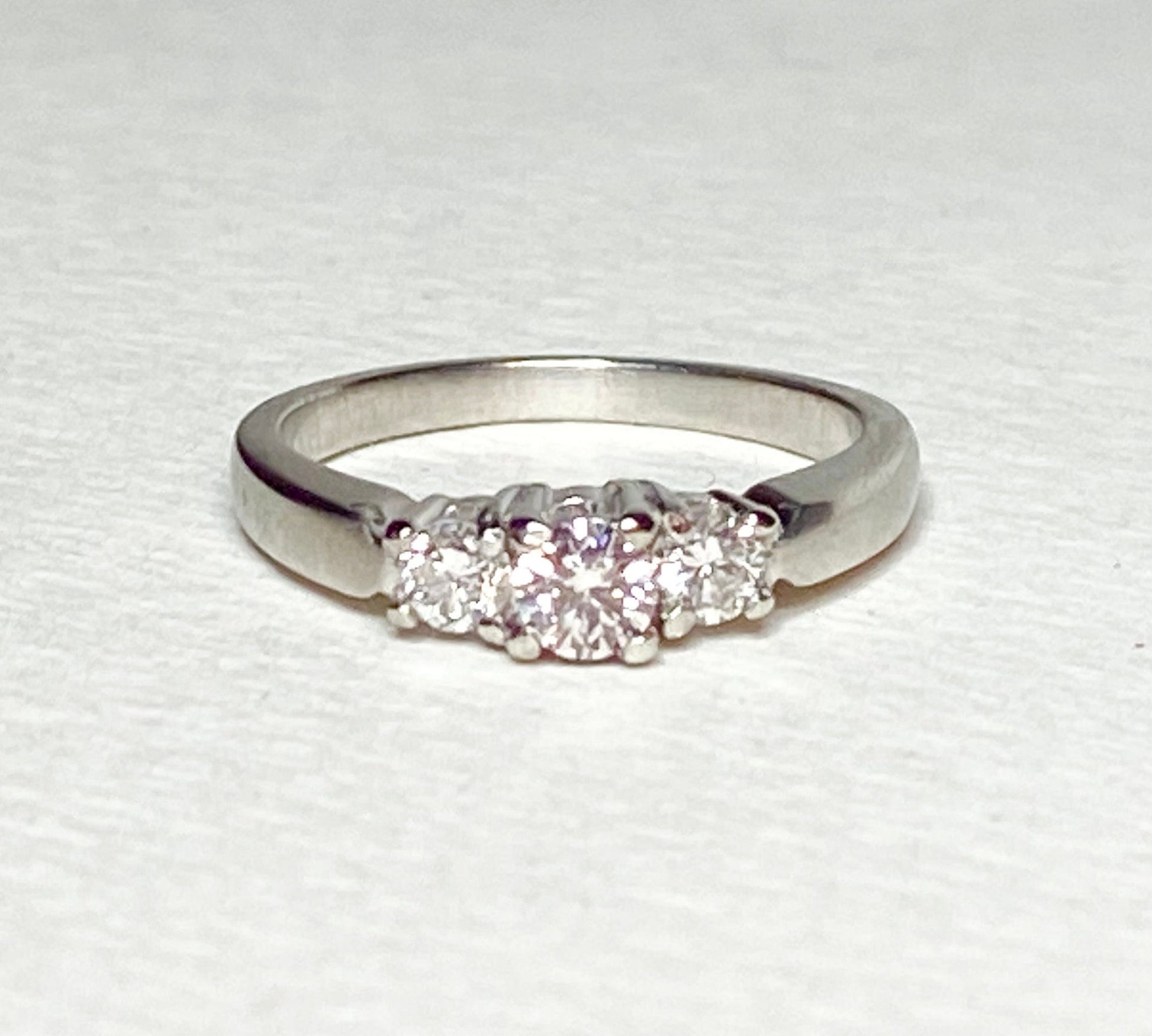 Platinum three-stone ring with a light pink diamond center and two white diamonds.