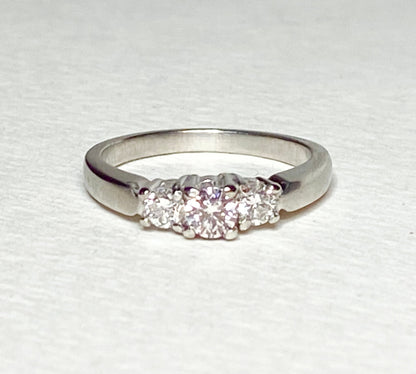 Platinum three-stone ring with a light pink diamond center and two white diamonds.